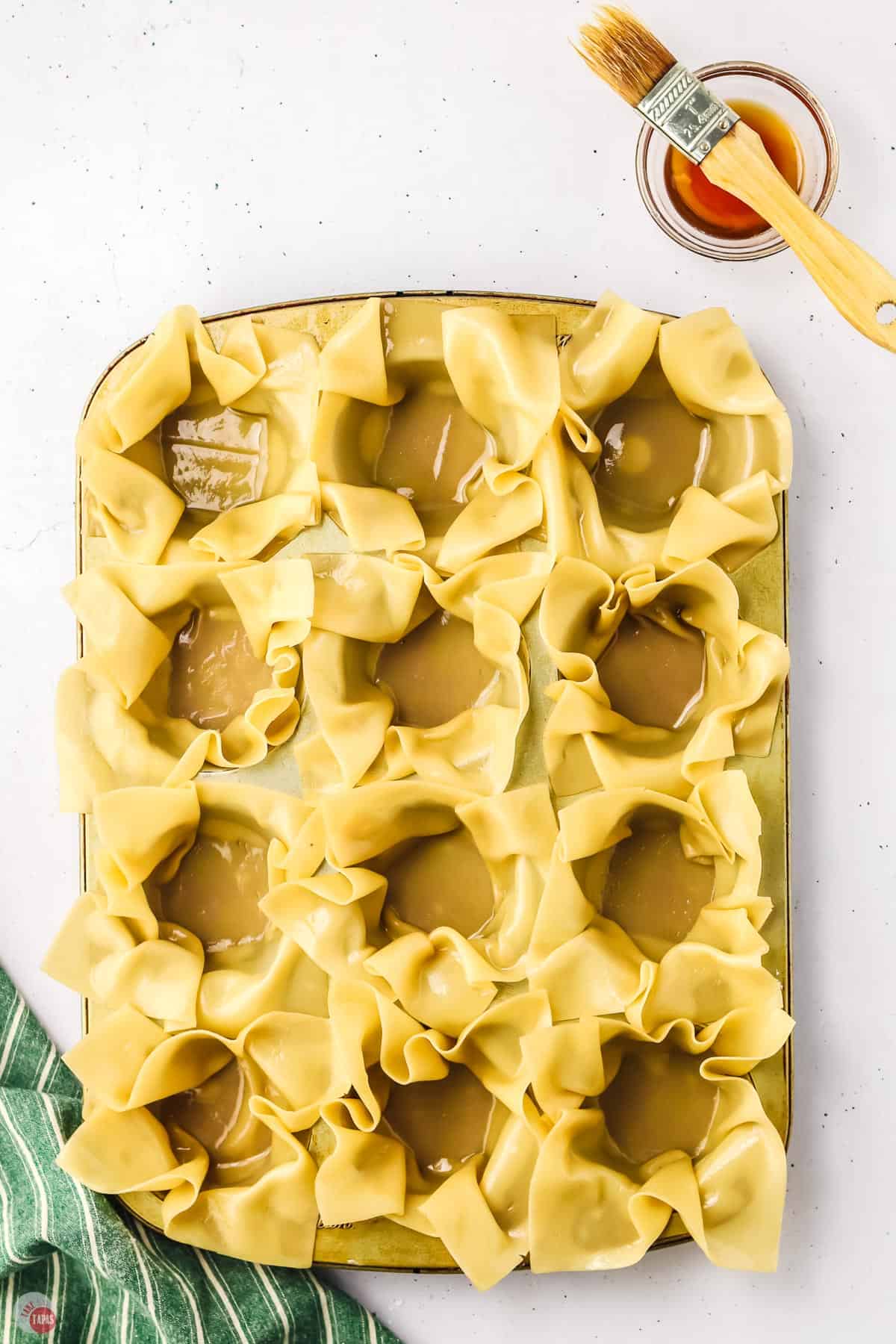 wonton wrappers being formed into cups in a muffin tin
