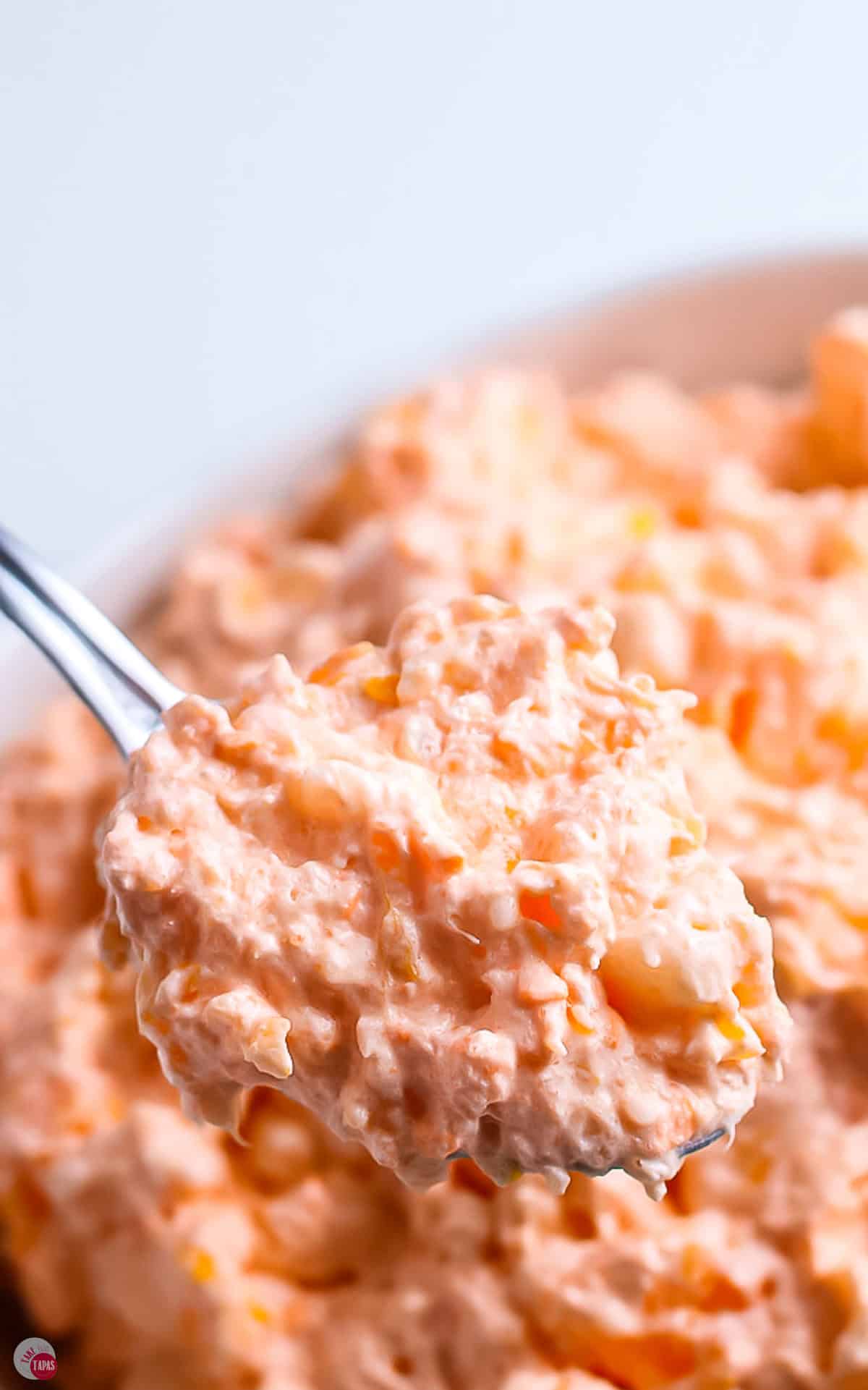 scoop of orange jello salad in a metal spoon