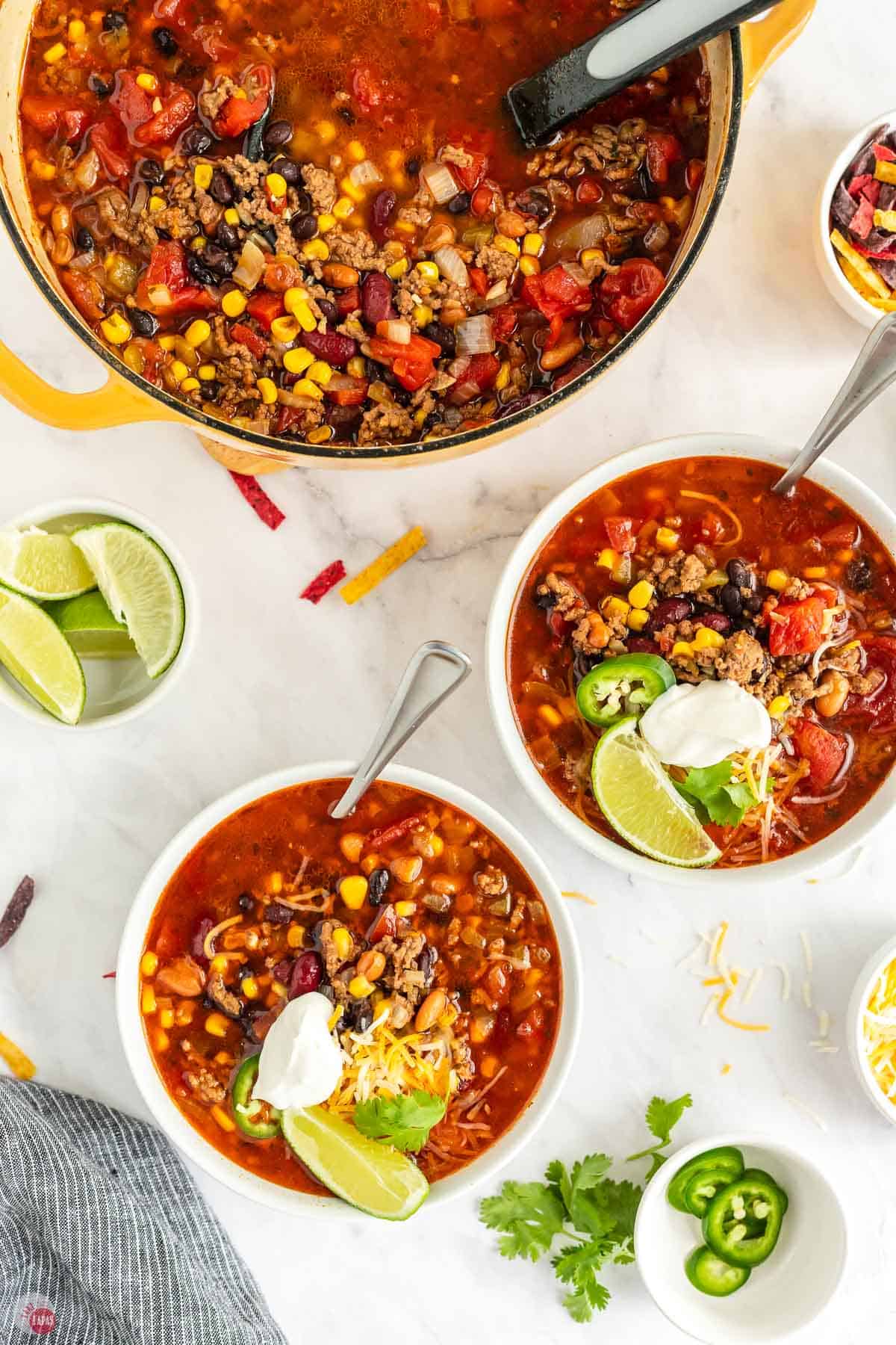 two bowls of soup next to a yellow pot with limes and sour cream