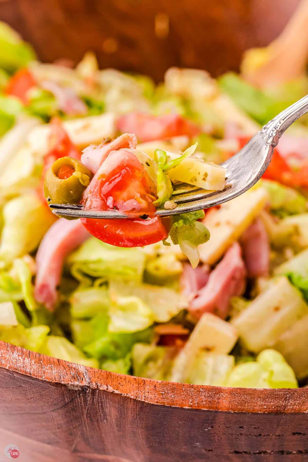 A fork is holding a salad with tomatoes and lettuce.