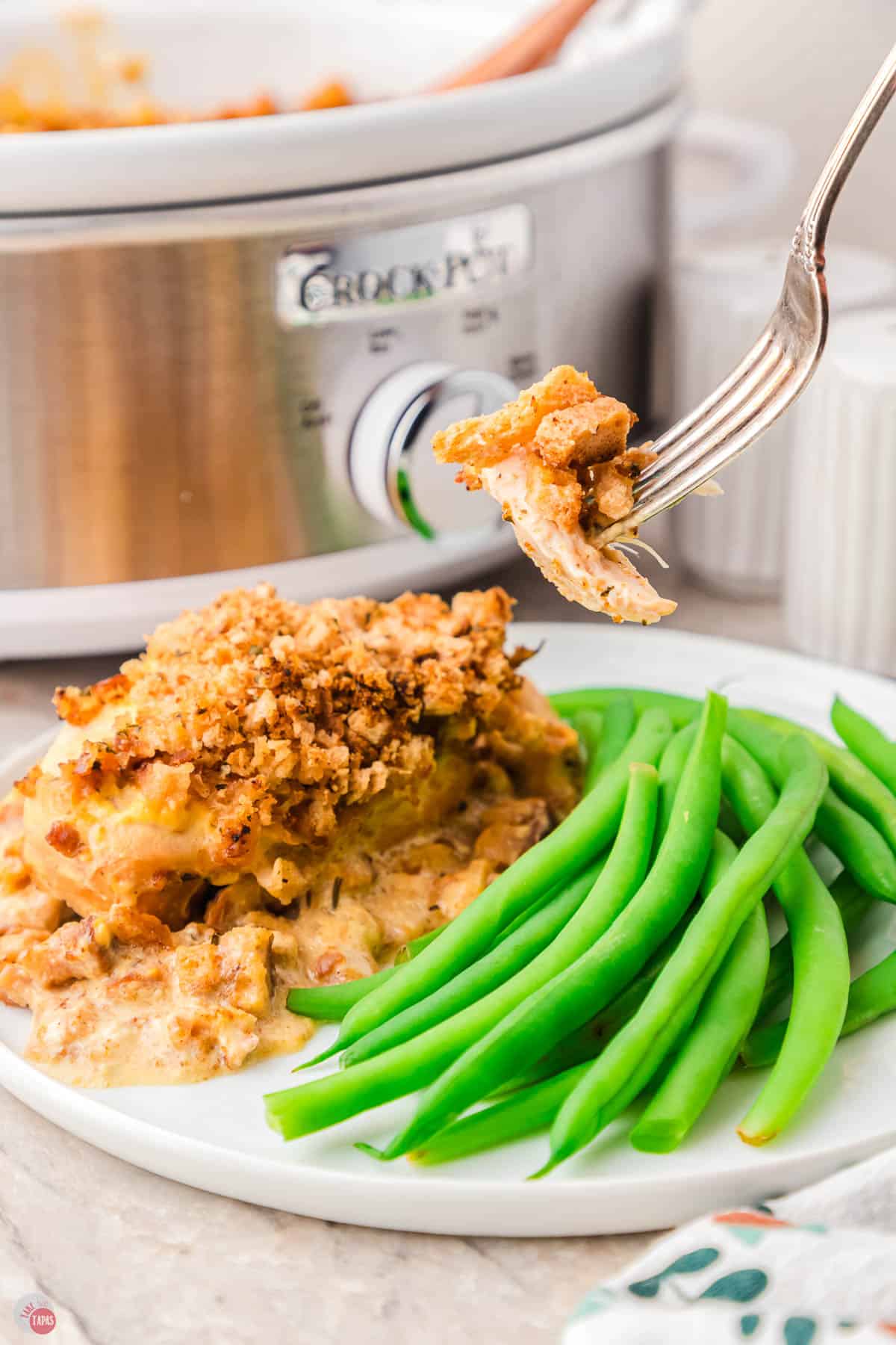 fork with bite of chicken on it over a plate of green beans