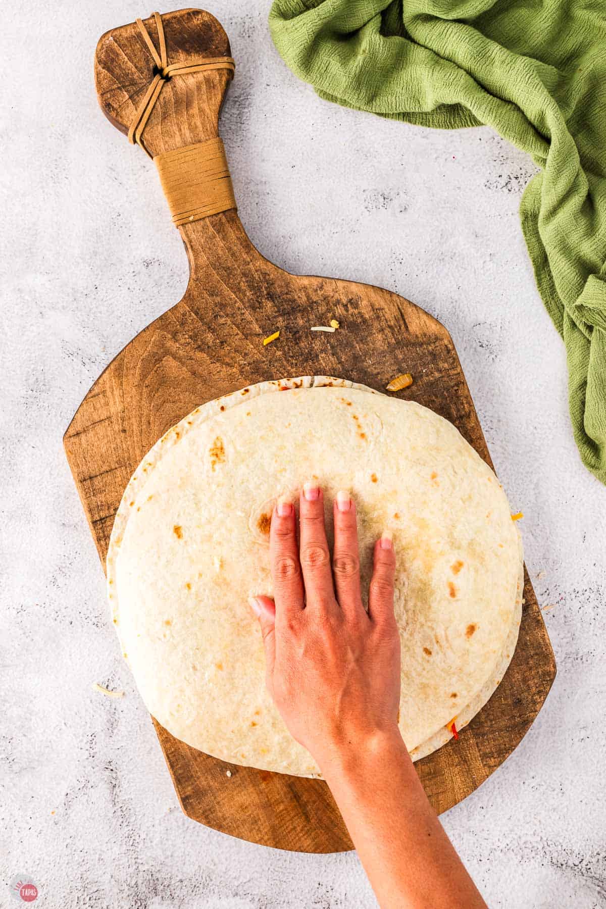 hand placing a flour tortilla on a wood board