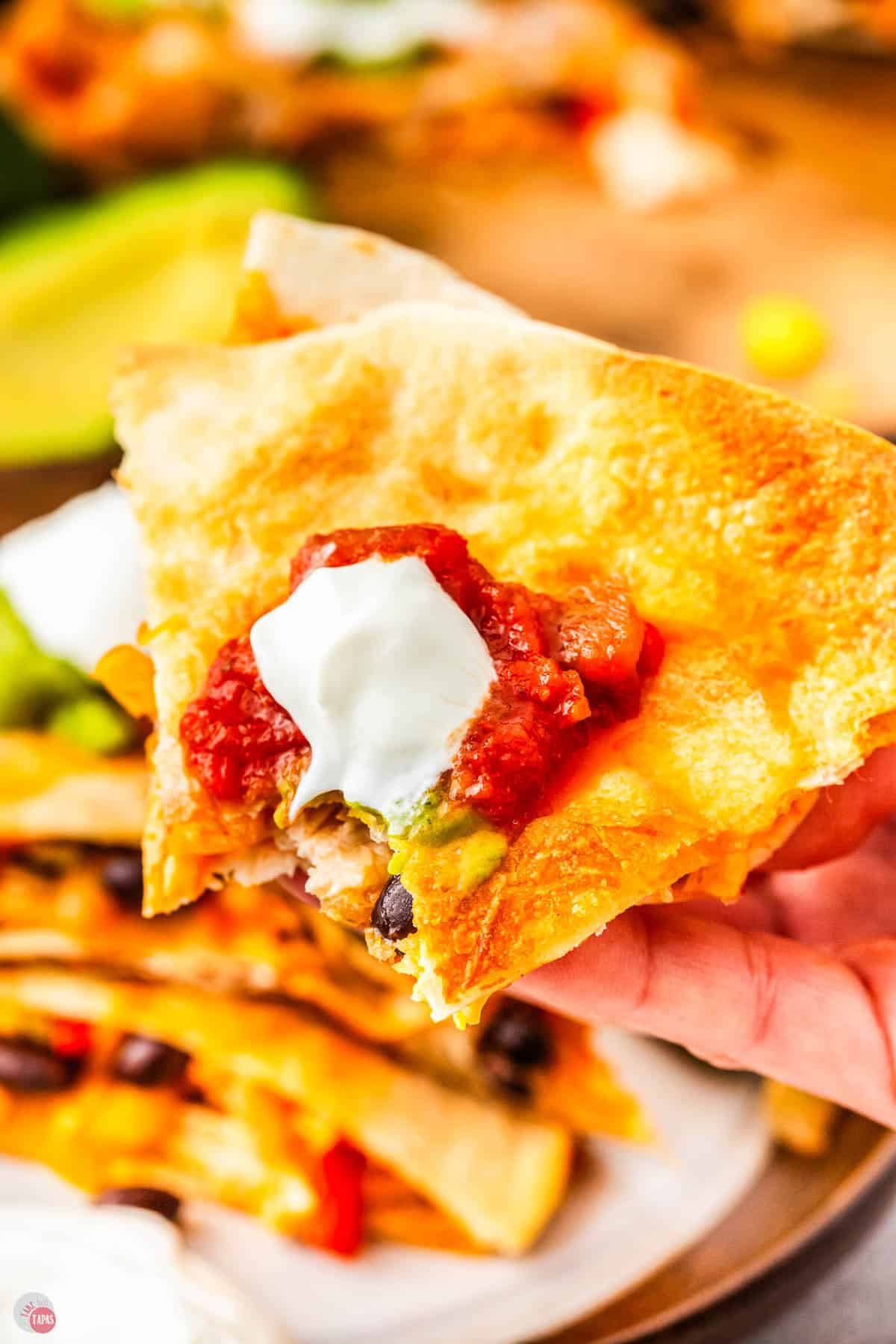 hand holding a quesadilla topped with sour cream and a bite missing