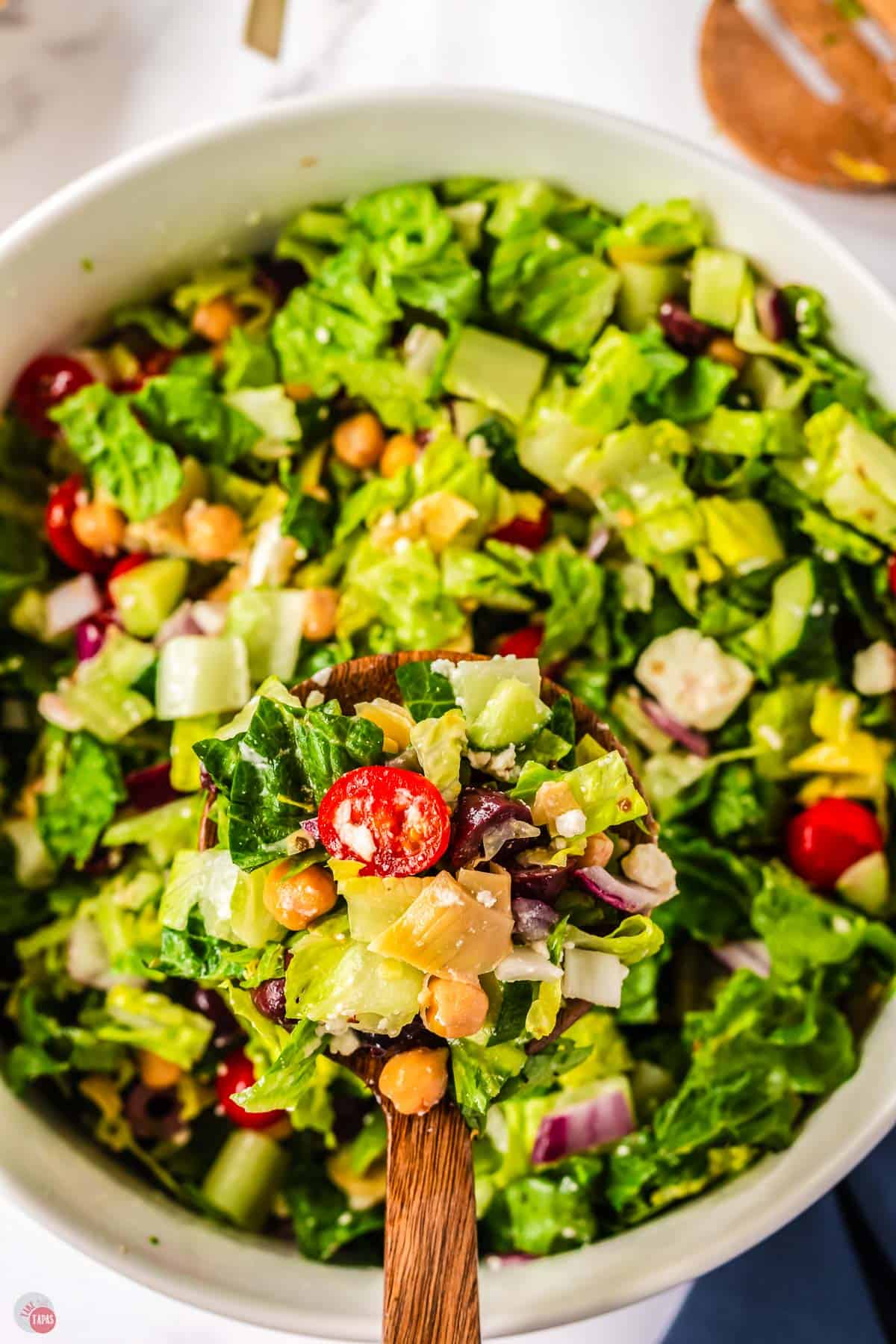 close up of bowl of salad with a scoop of it on a wood spoon