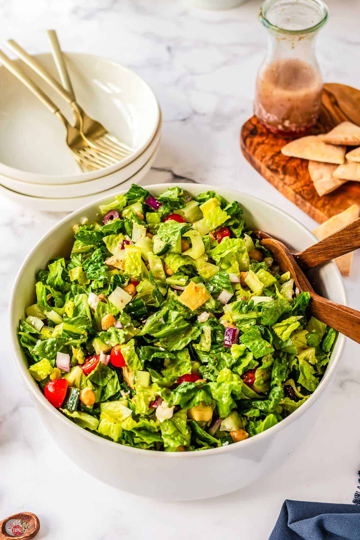 salad being mixed in a white bowl with wood spoons
