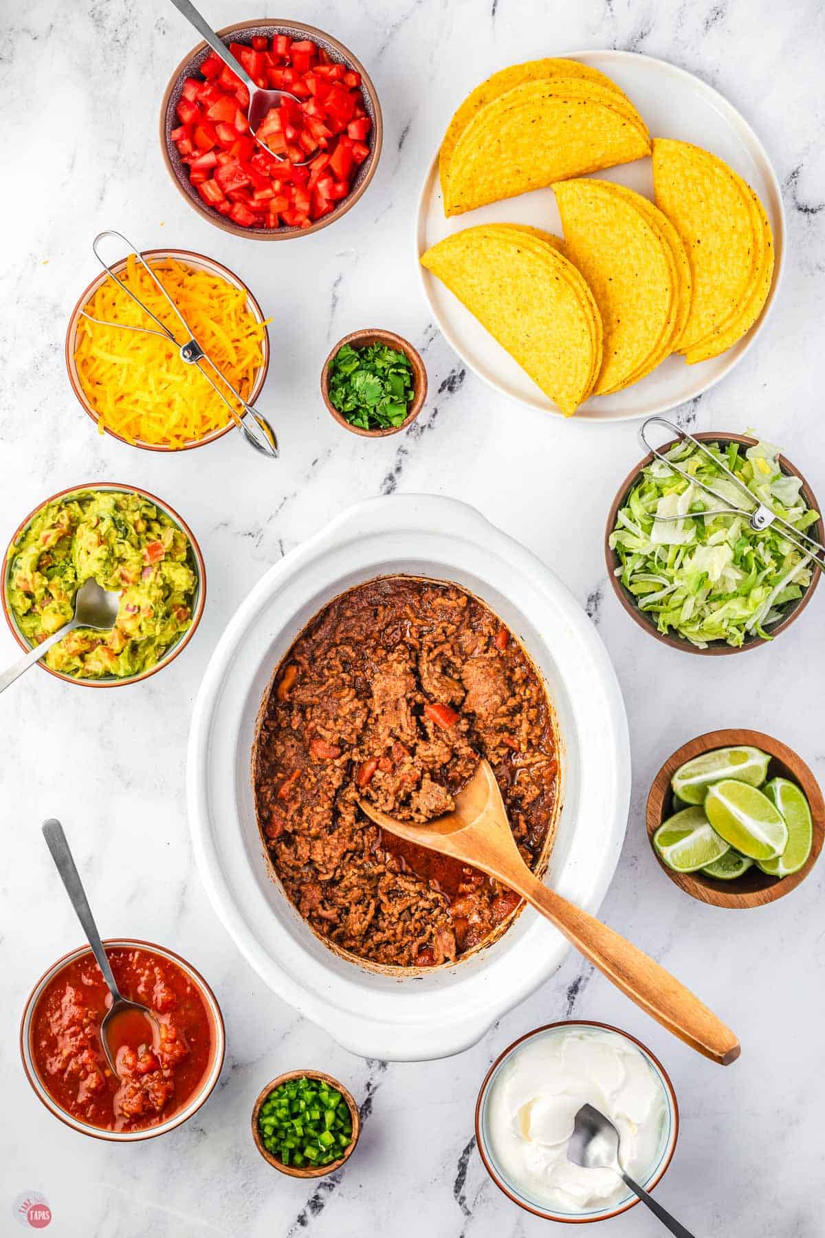 bowl of taco meat surrounded by bowls of toppings and taco shells