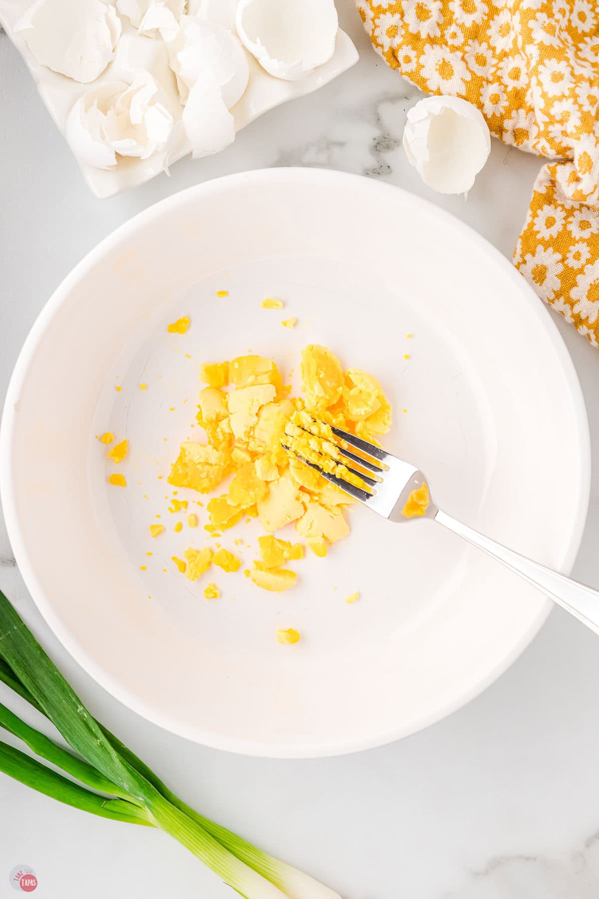 fork mashing an egg yolk in a white bowl