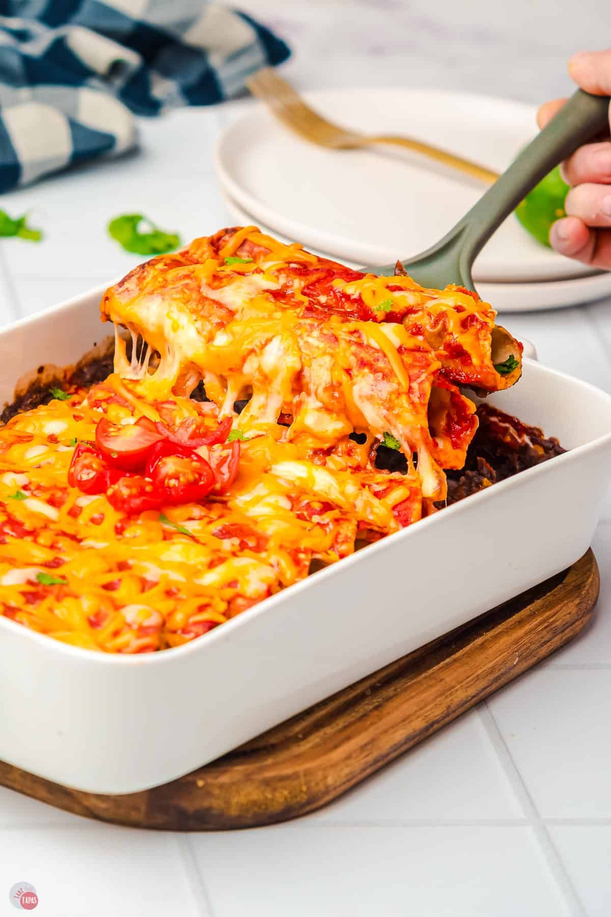 spatula scooping enchiladas out of a white dish