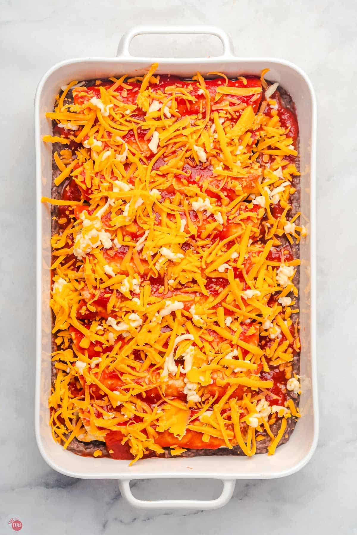 enchiladas in a baking dish topped shredded cheese
