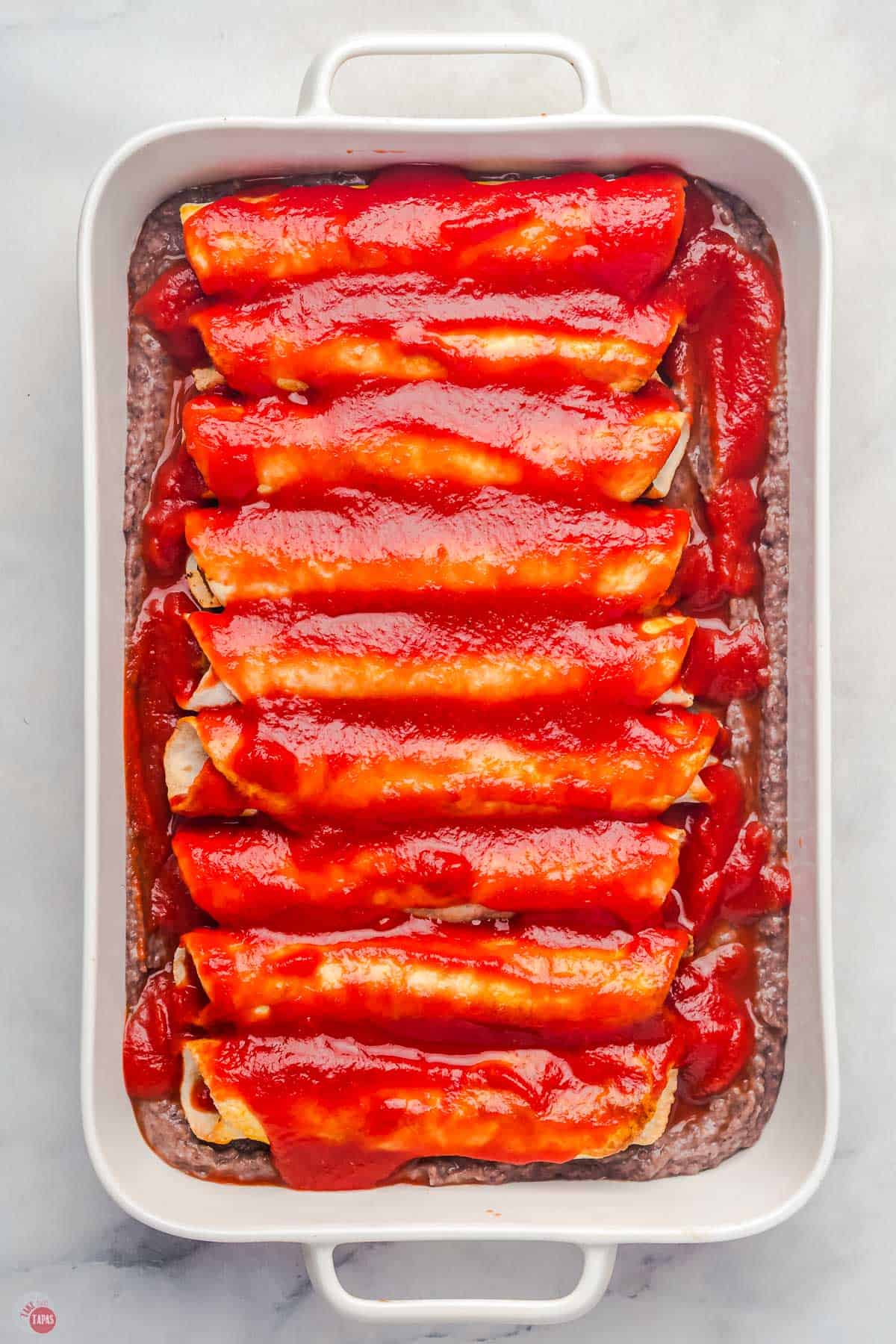 taquitos in a dish topped with red enchilada sauce