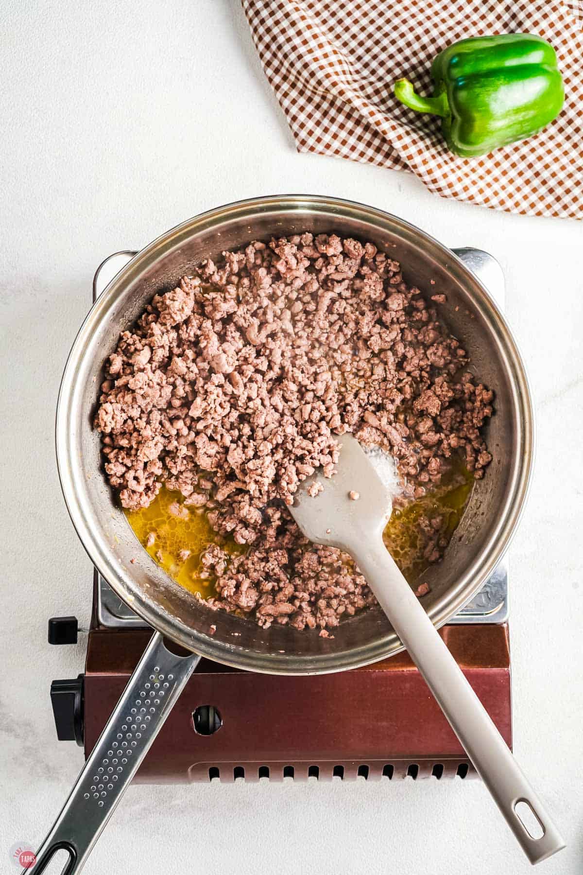 ground beef browning in a skillet with a gray spatula