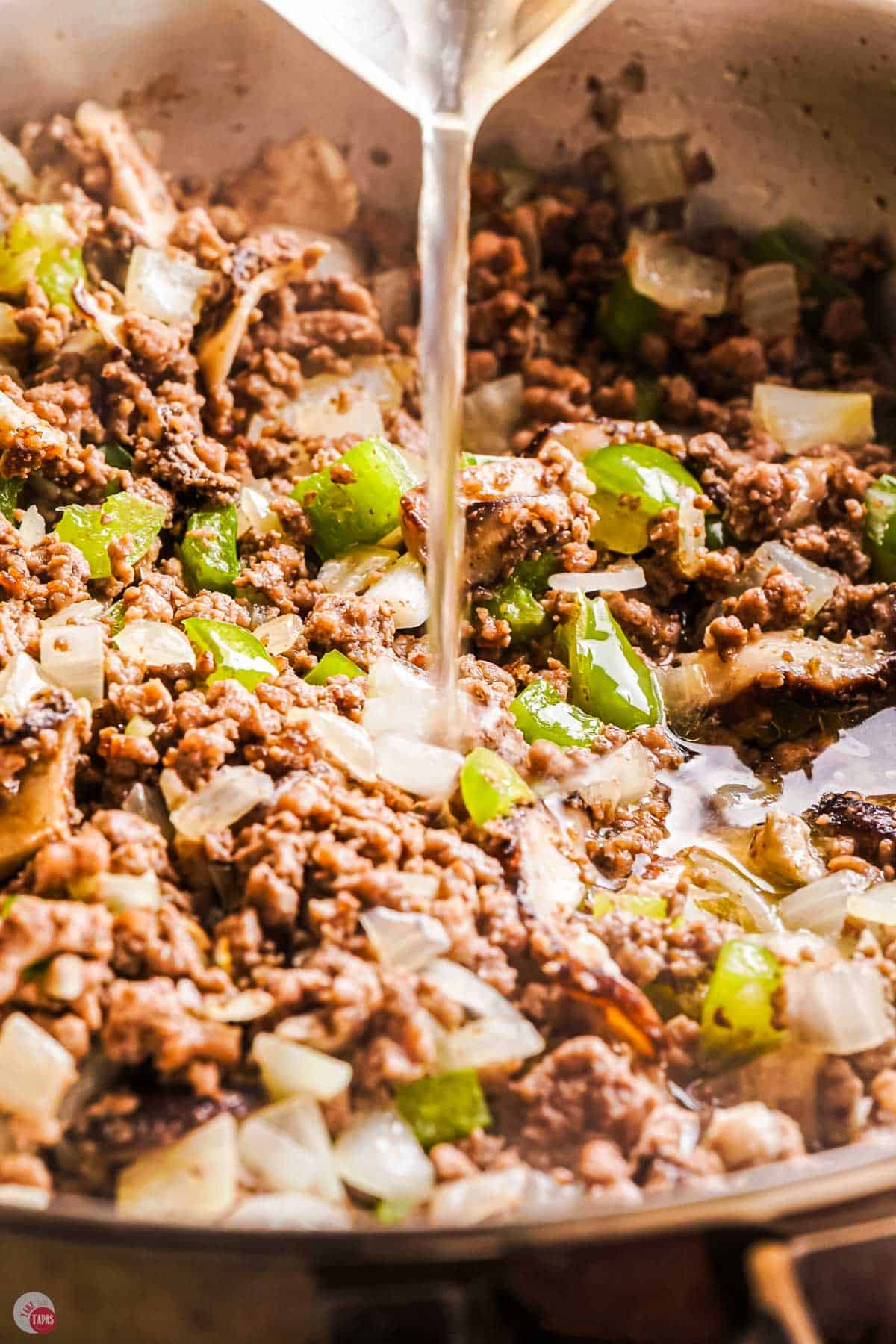 close up of ground beef with seasoning and broth cooking in a skillet