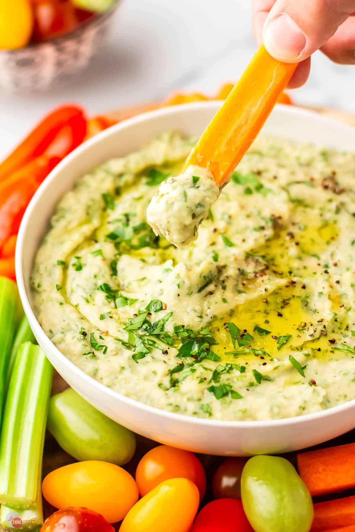 carrot stick scooping out some hummus topped with parsley