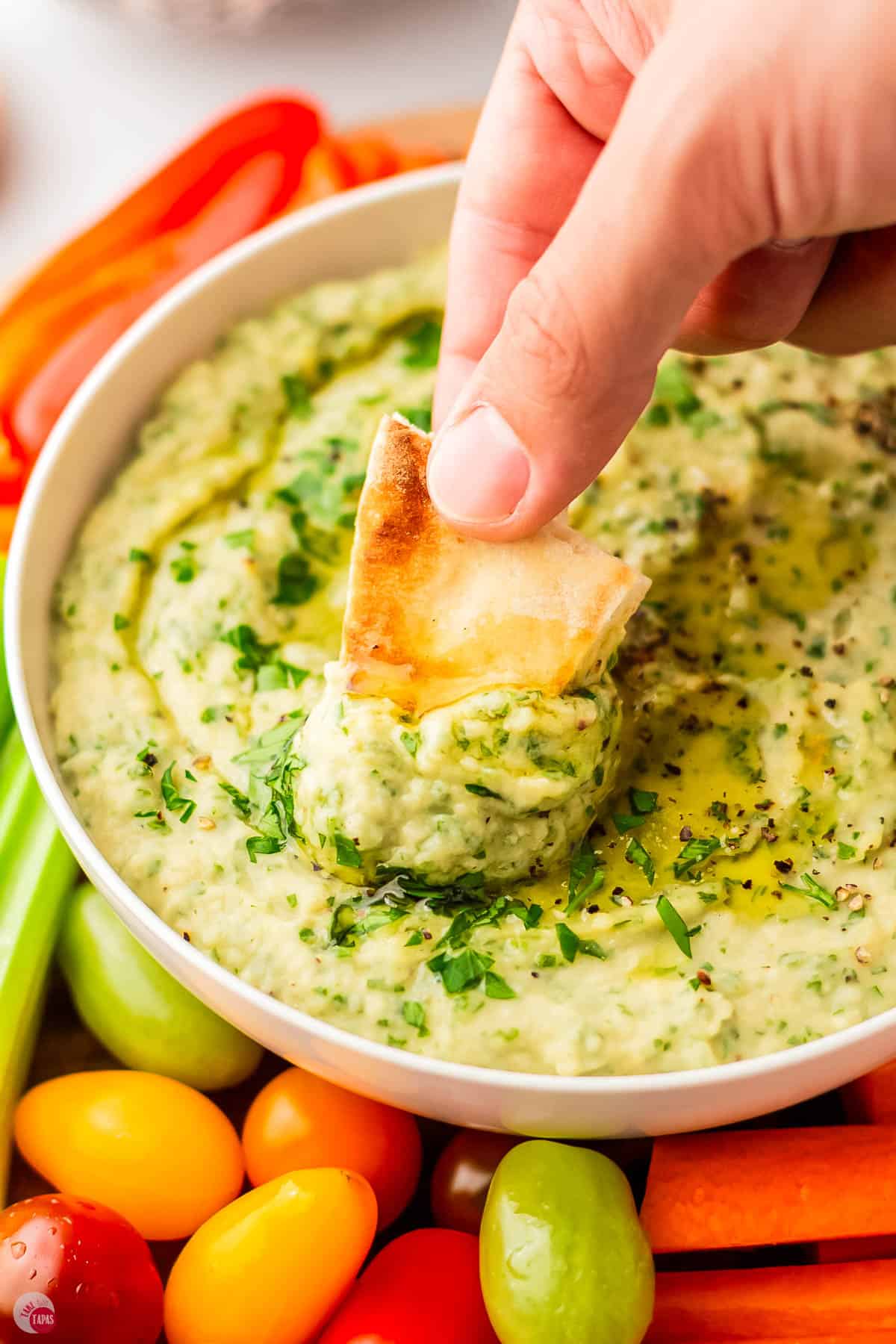 hand scooping hummus out of a bowl with a pita chip