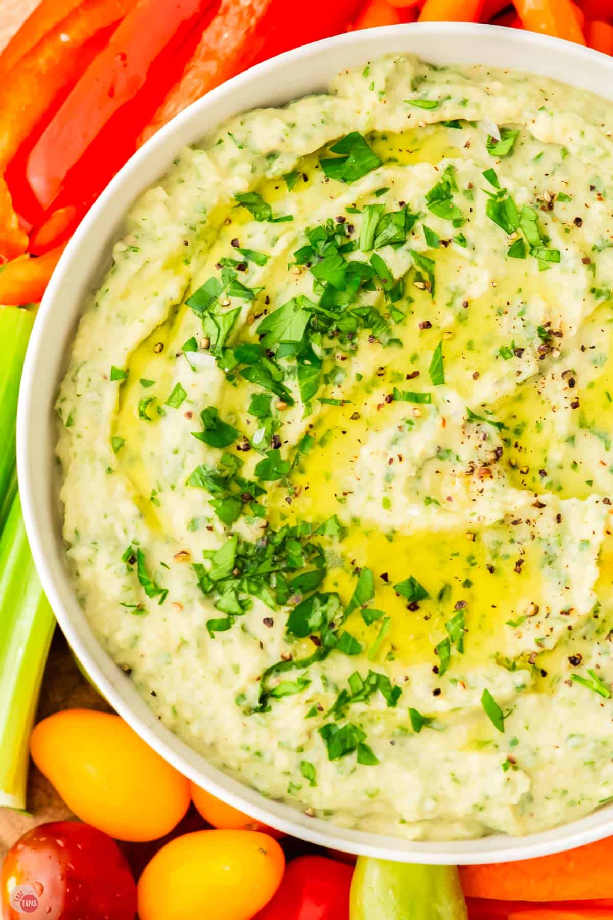 close up of bowl of white bean hummus topped with olive oil and chopped parsley