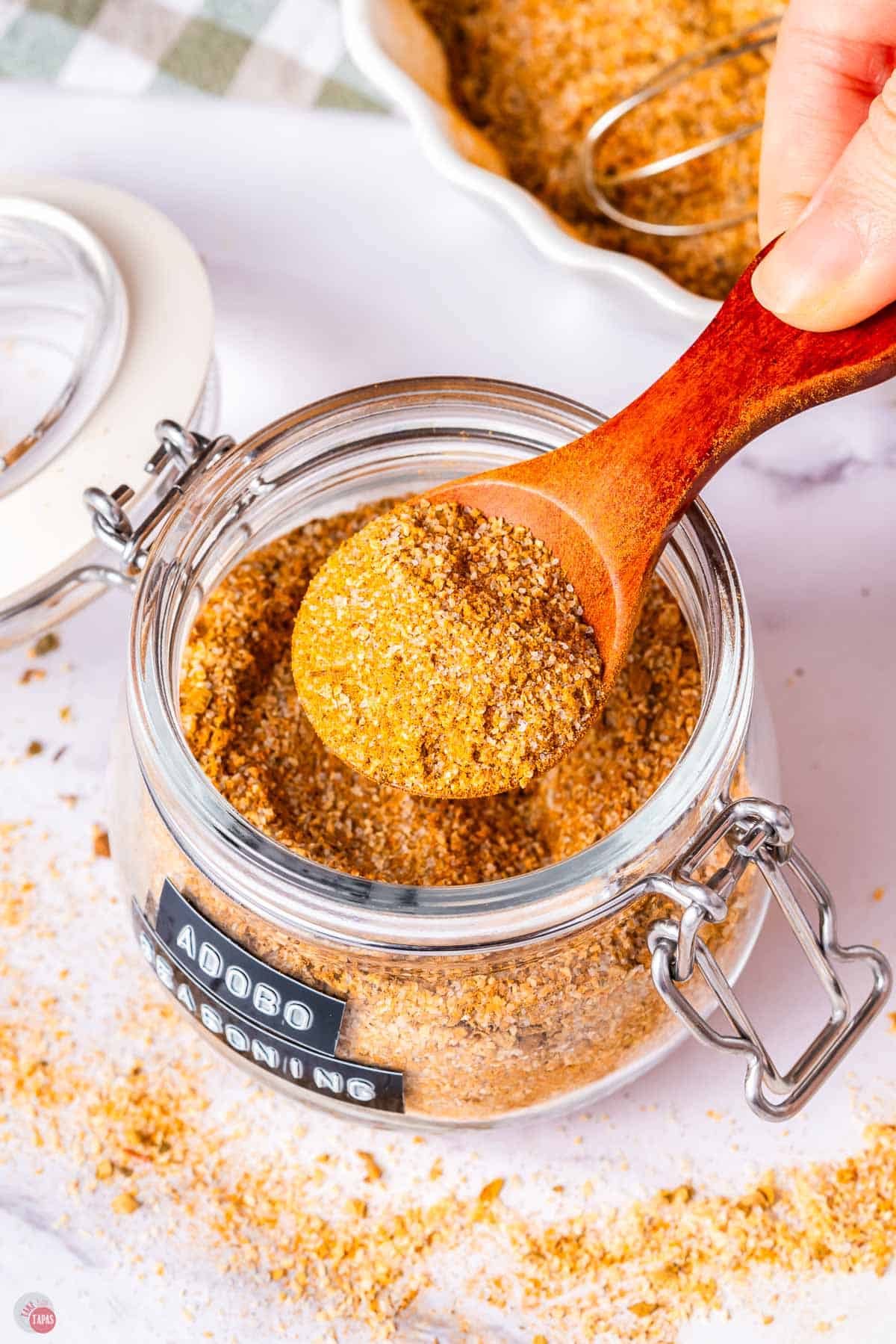 jar of Adobo seasoning with a wood spoon scooping some out