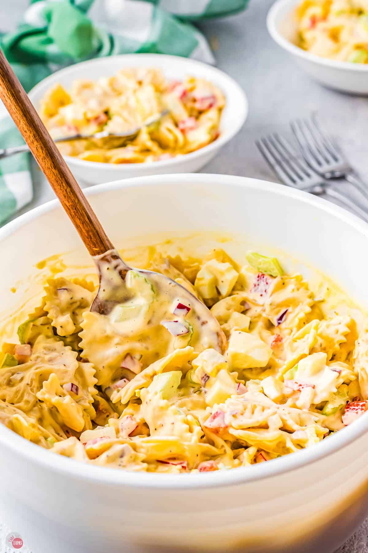 close up of bowl of pasta salad with wood spoon in it