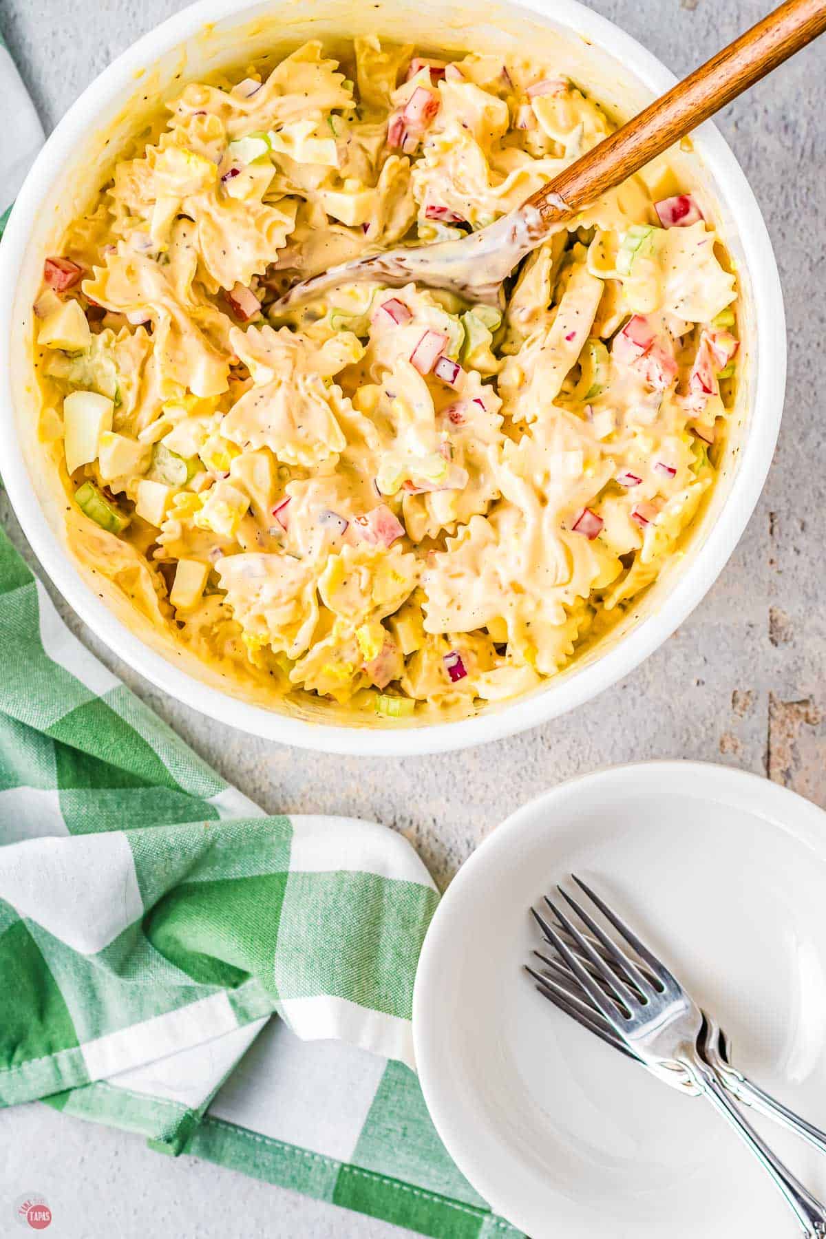 large bowl of pasta salad next to small white bowl with two forks in it