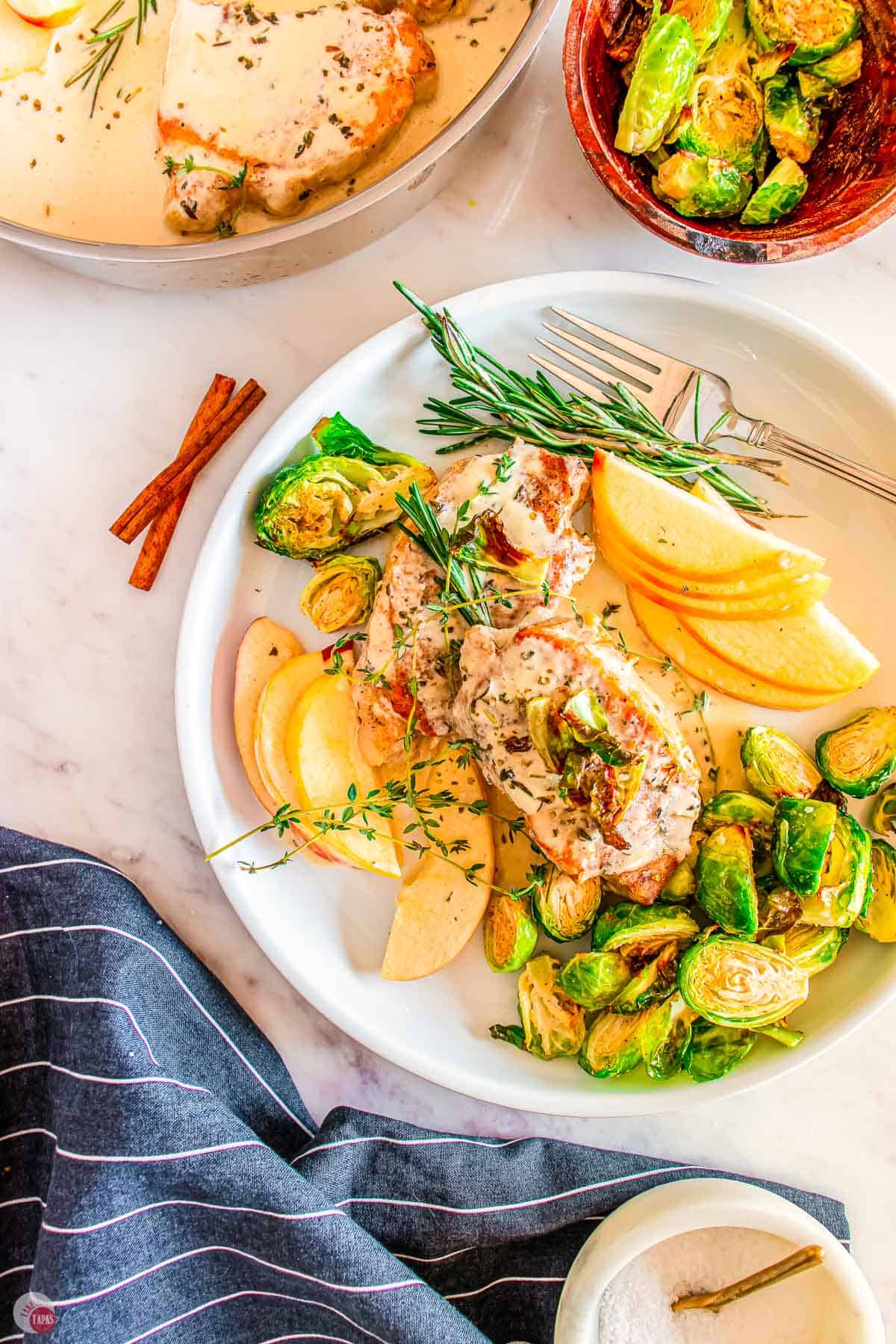 two white plates with pork chops and apples on it