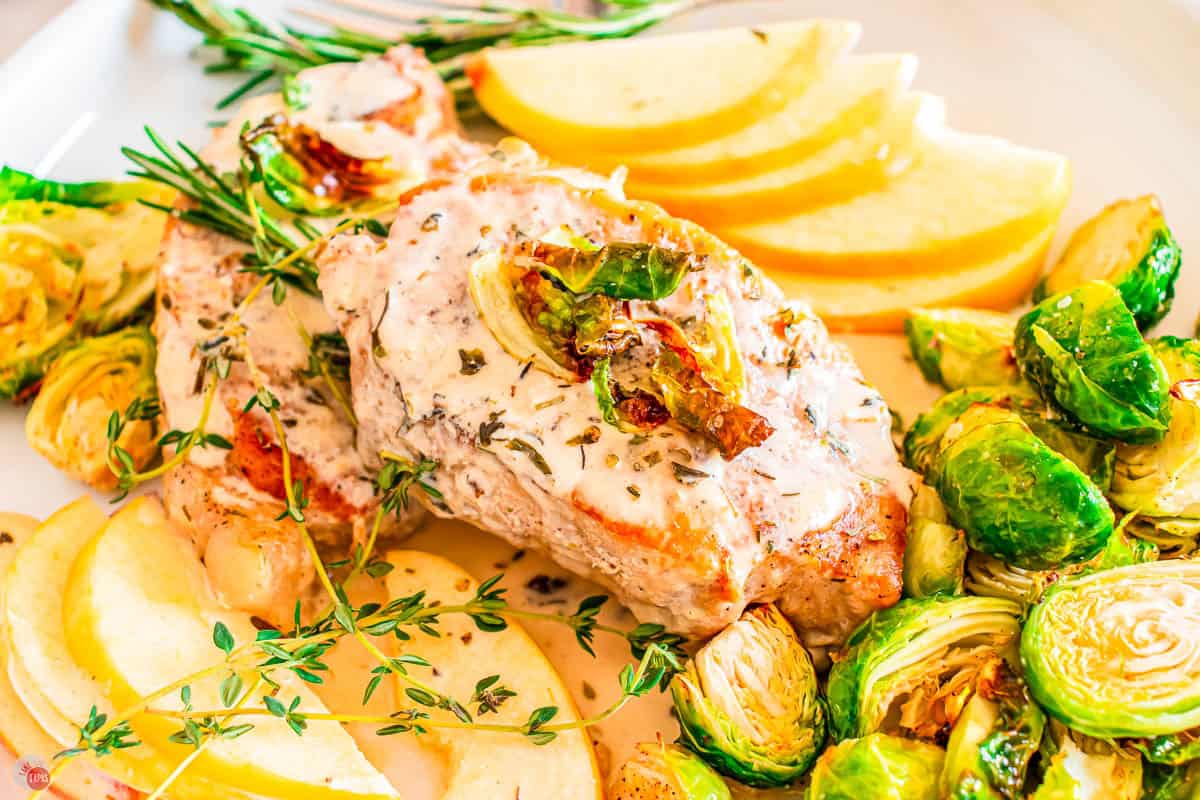 close up of pork chop on a plate with apple slices and sprouts