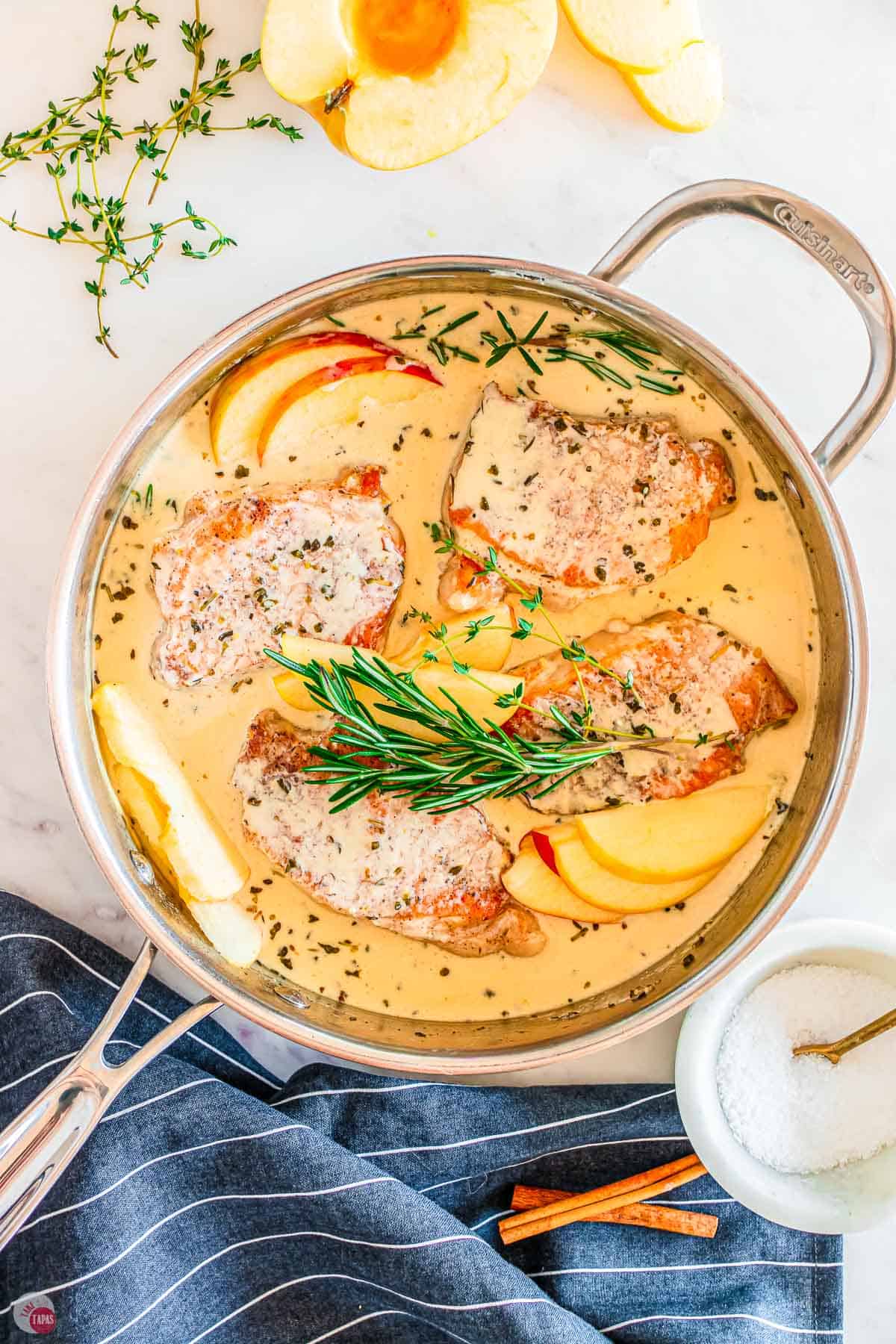 skillet with sauce, pork chops, and fresh herbs in it