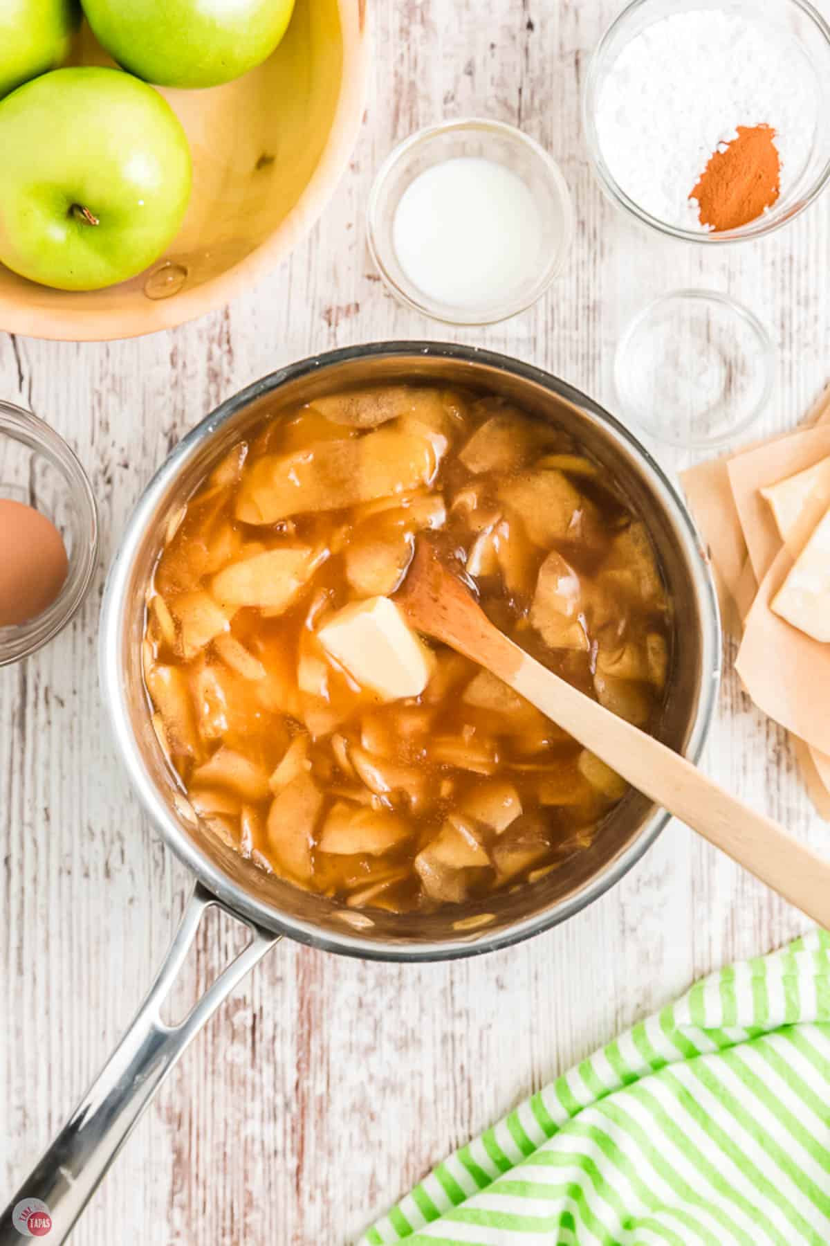 wood spoon stirring butter into a pot of apples