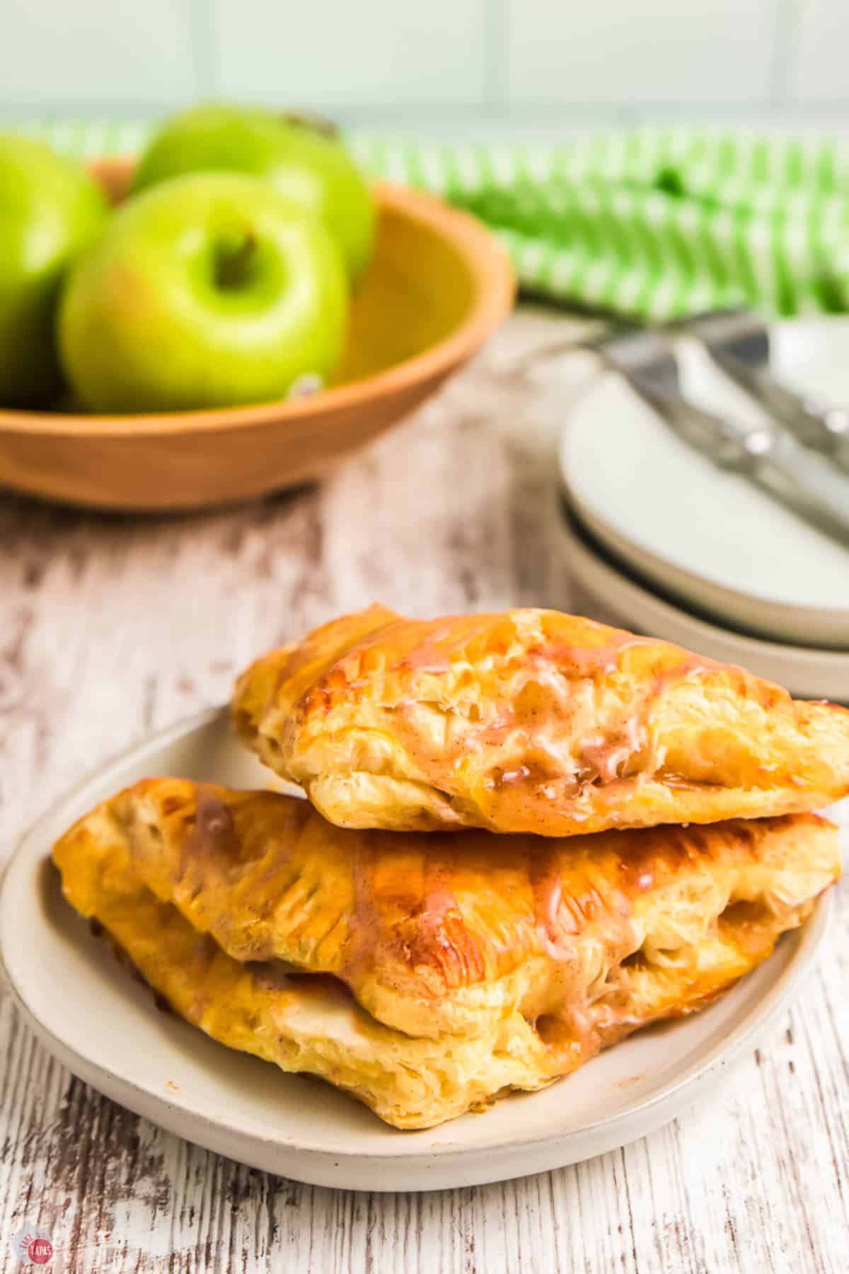 plate of two apple turnovers with a bowl of apples in the background