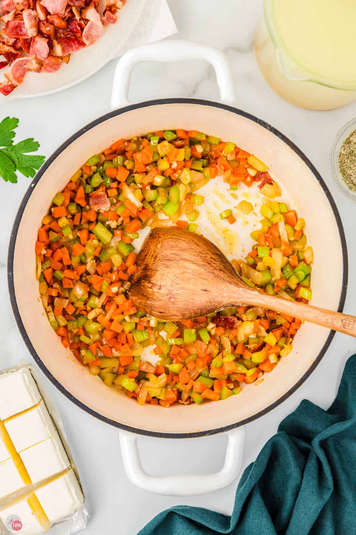 carrots, onion, and celery cooking in a white pot with a wood spoon