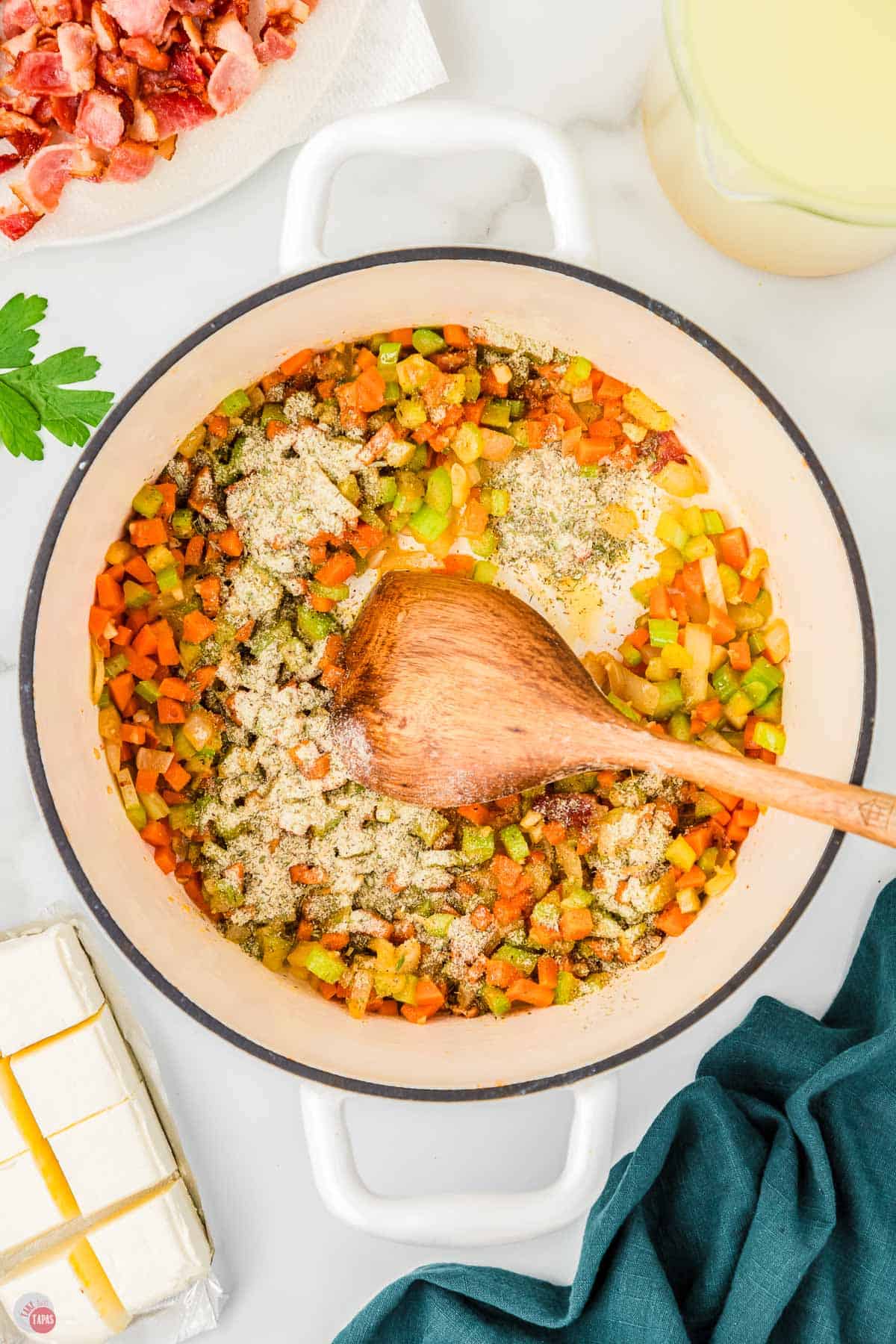 carrots and celery cooking in a white pot with a wood spoon