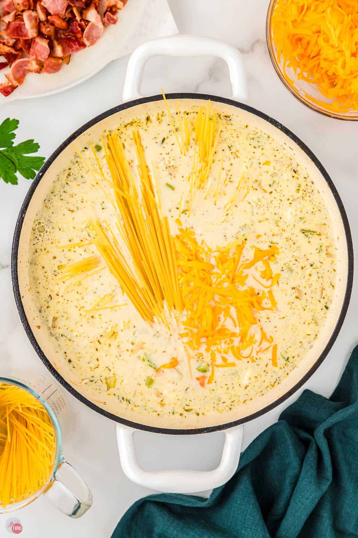 soup pot with cream broth and dry noodles being added in