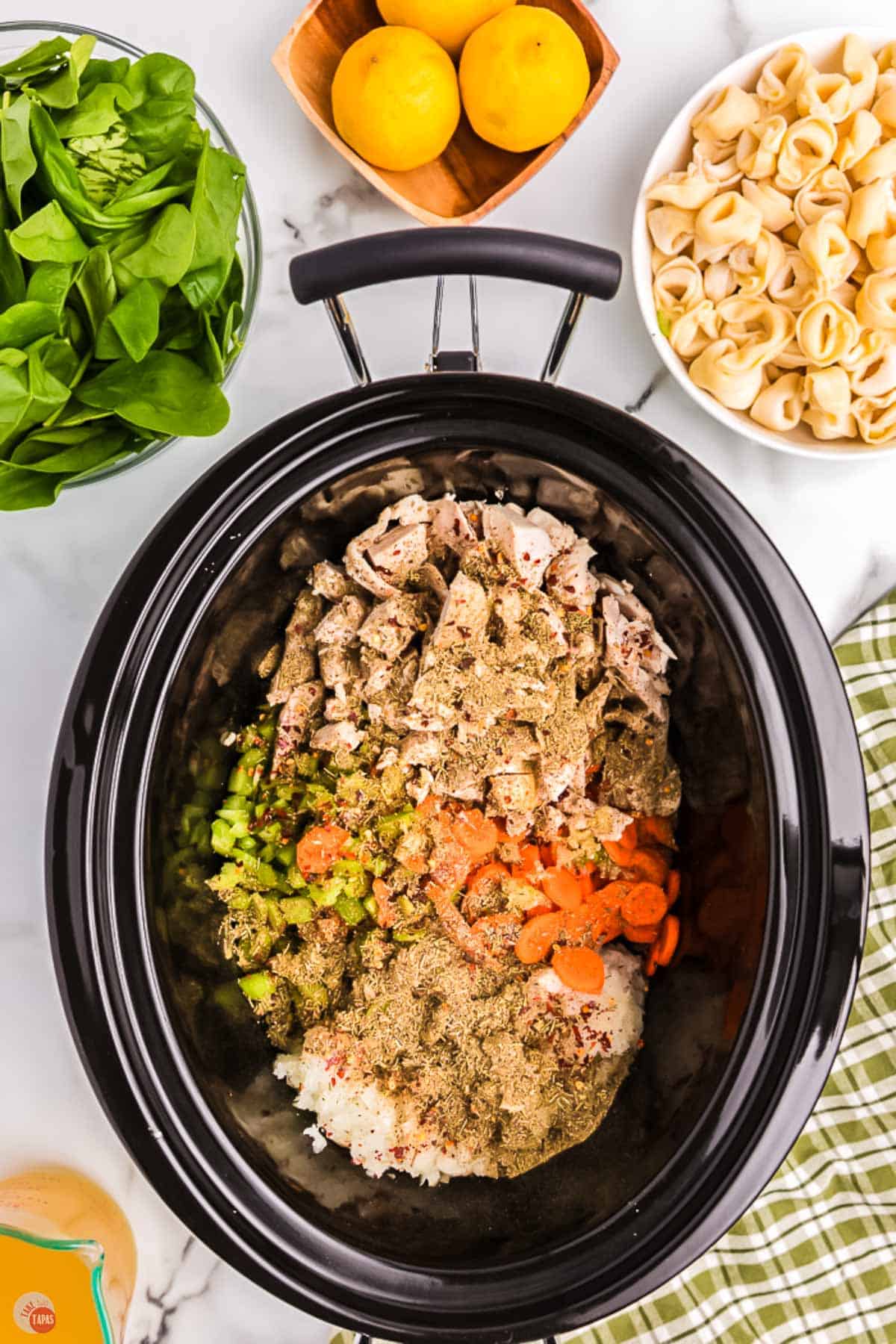 chicken, vegetables, and spices in a black slow cooker pot