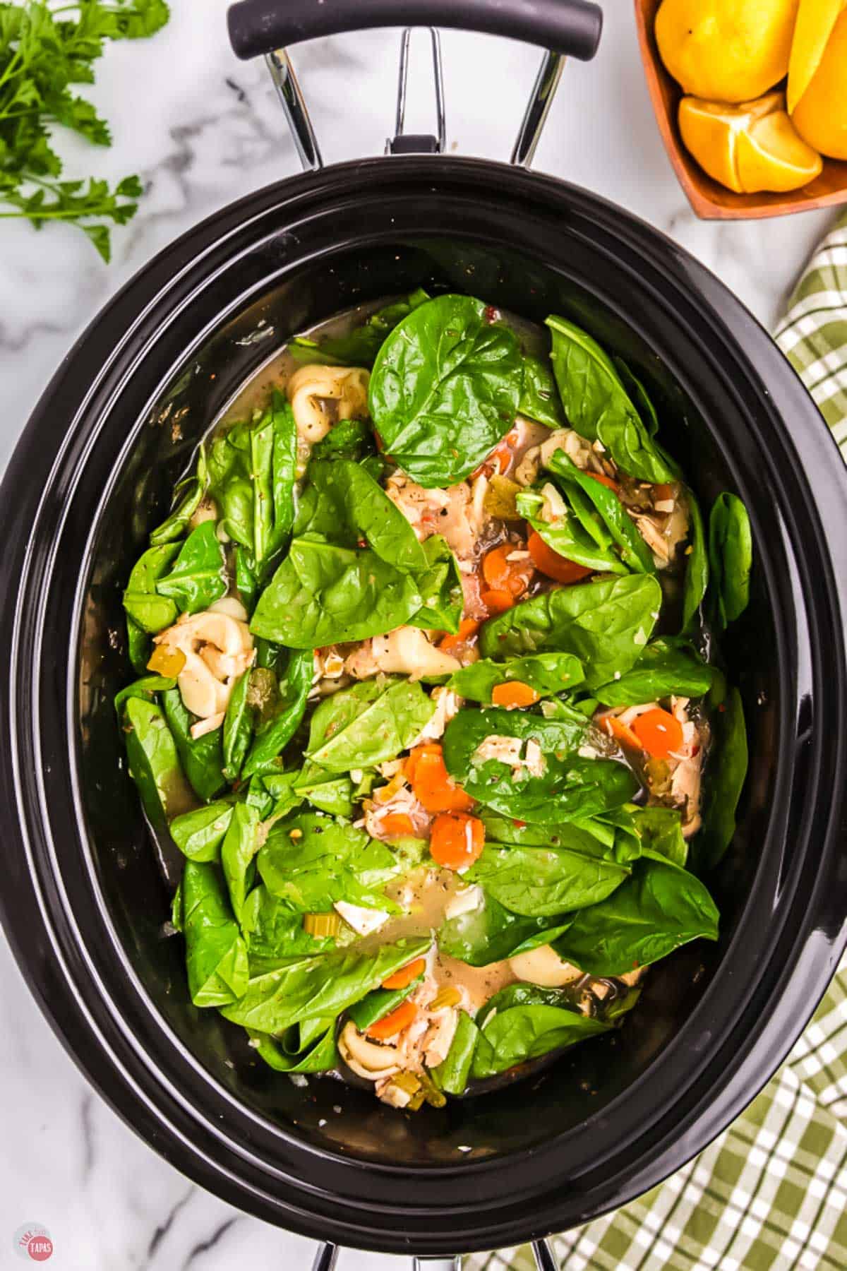 soup in a slow cooker with fresh spinach on top