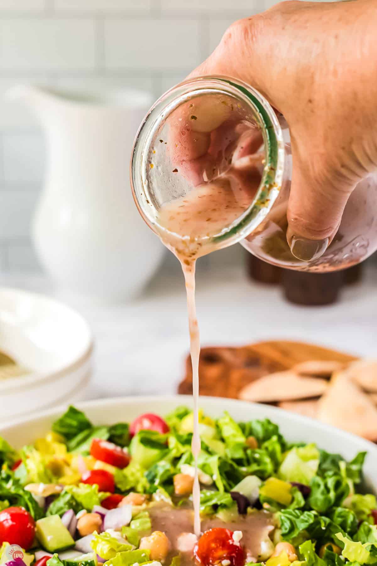 hand holding jar pouring dressing onto a salad