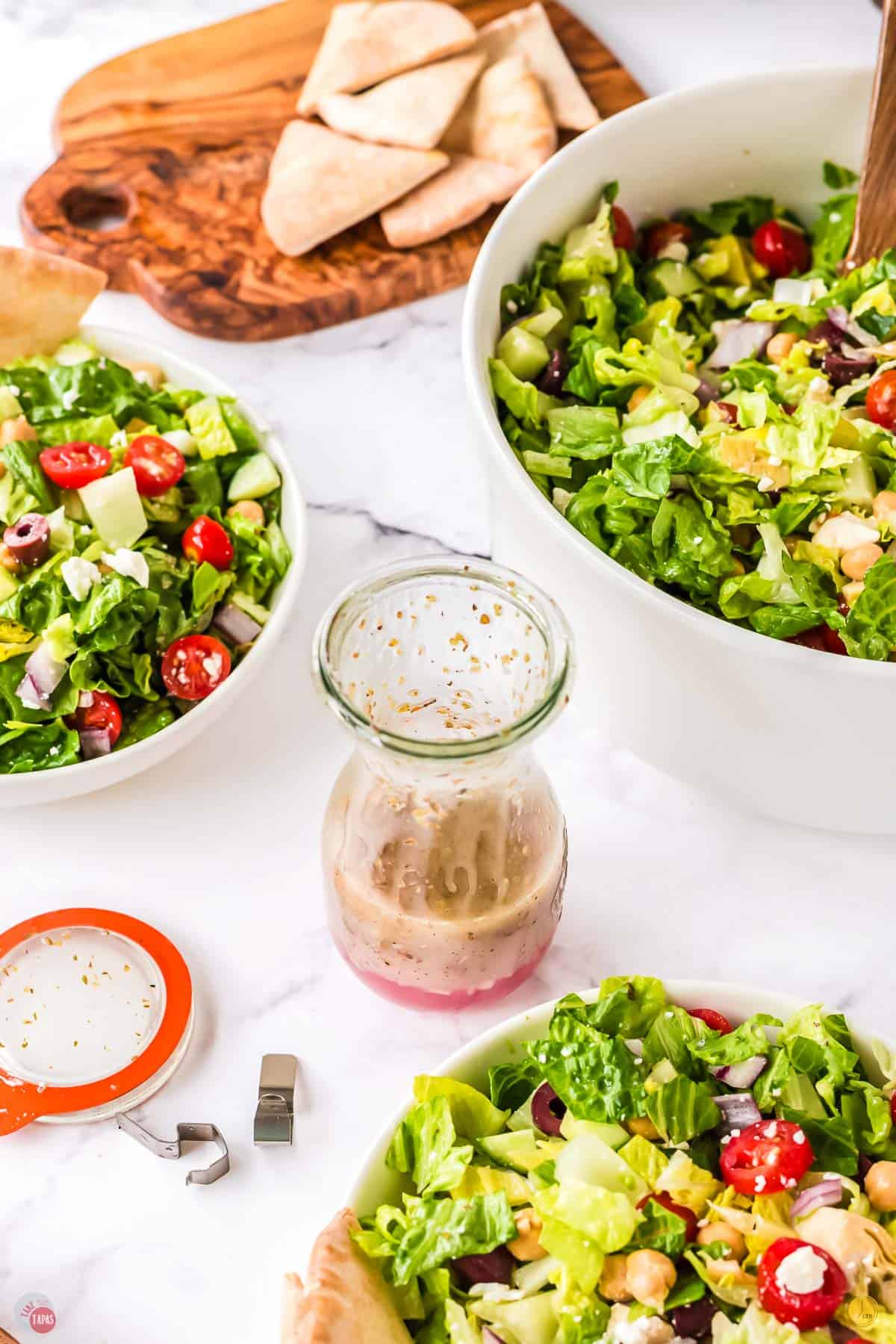 three bowls of salad with a half empty jar of dressing in the middle