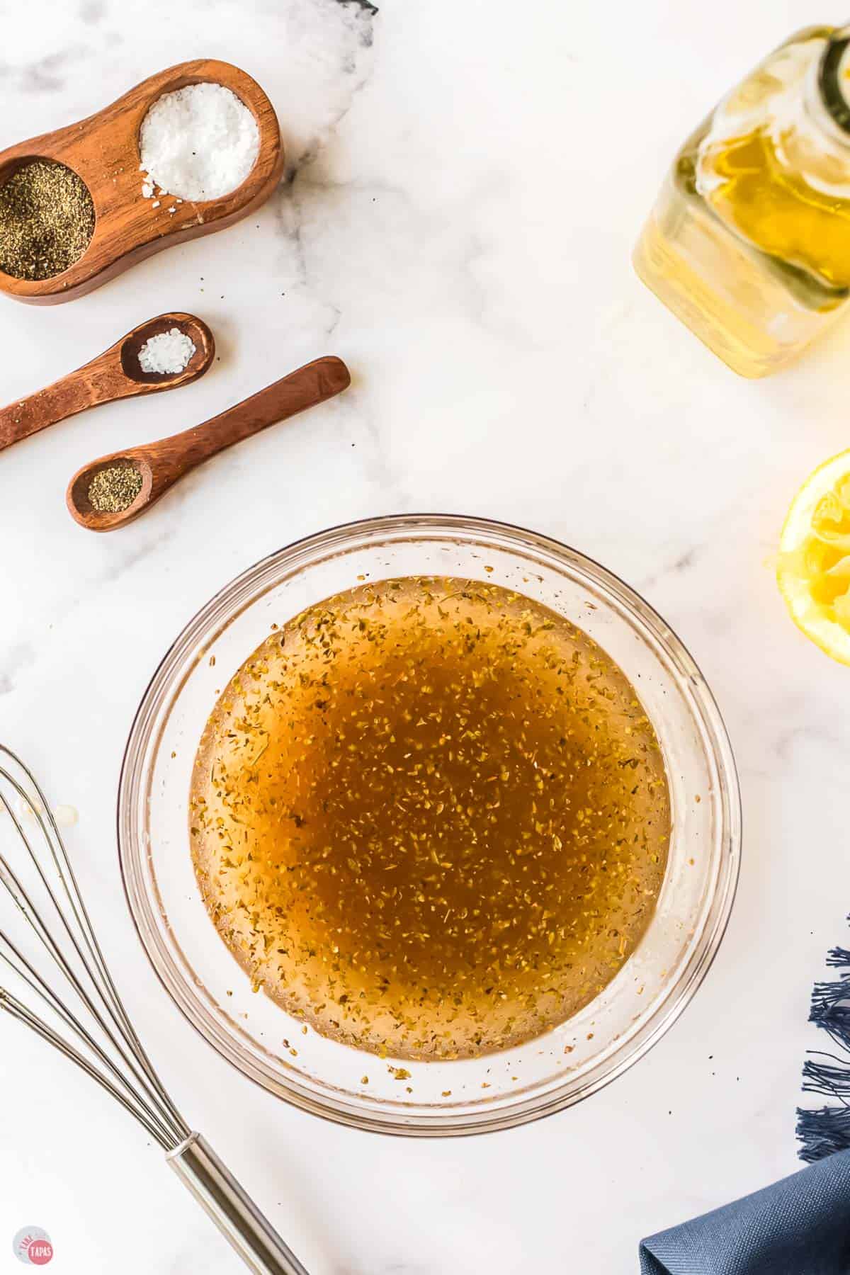 greek salad dressing in a clear bowl with a whisk