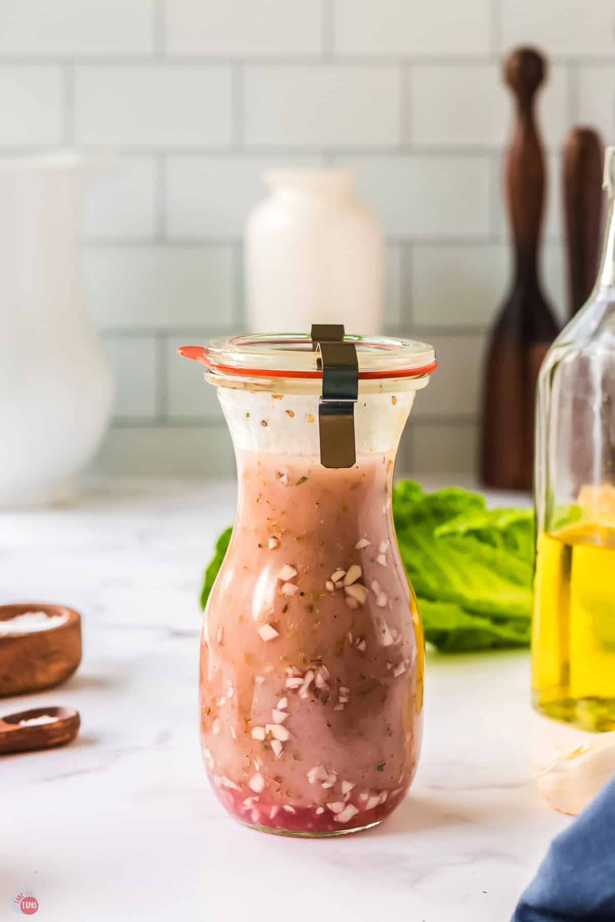Jar of salad dressing on a counter with lettuce behind it