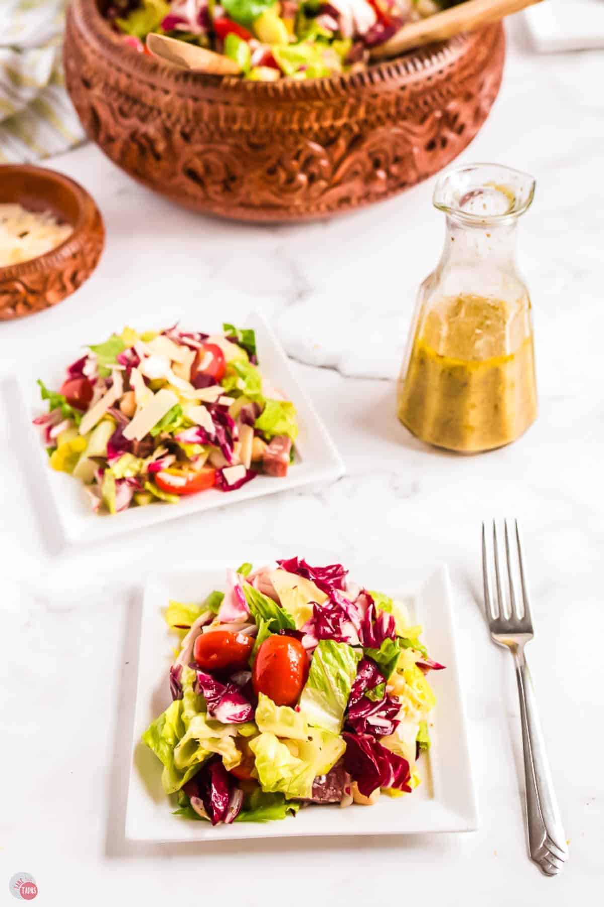 two plates of salad with a jar of dressing next to it
