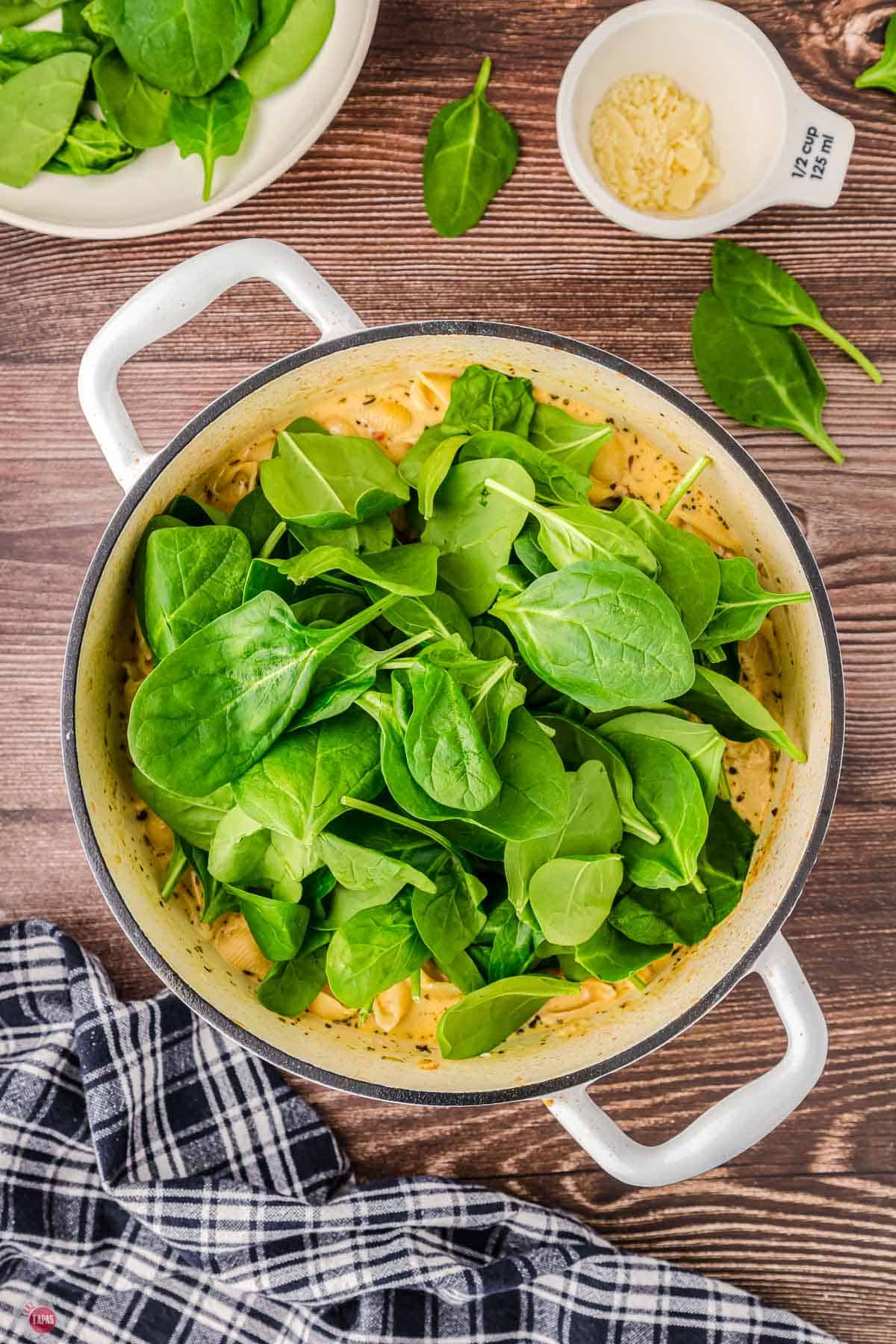 soup pot with fresh spinach being added to it