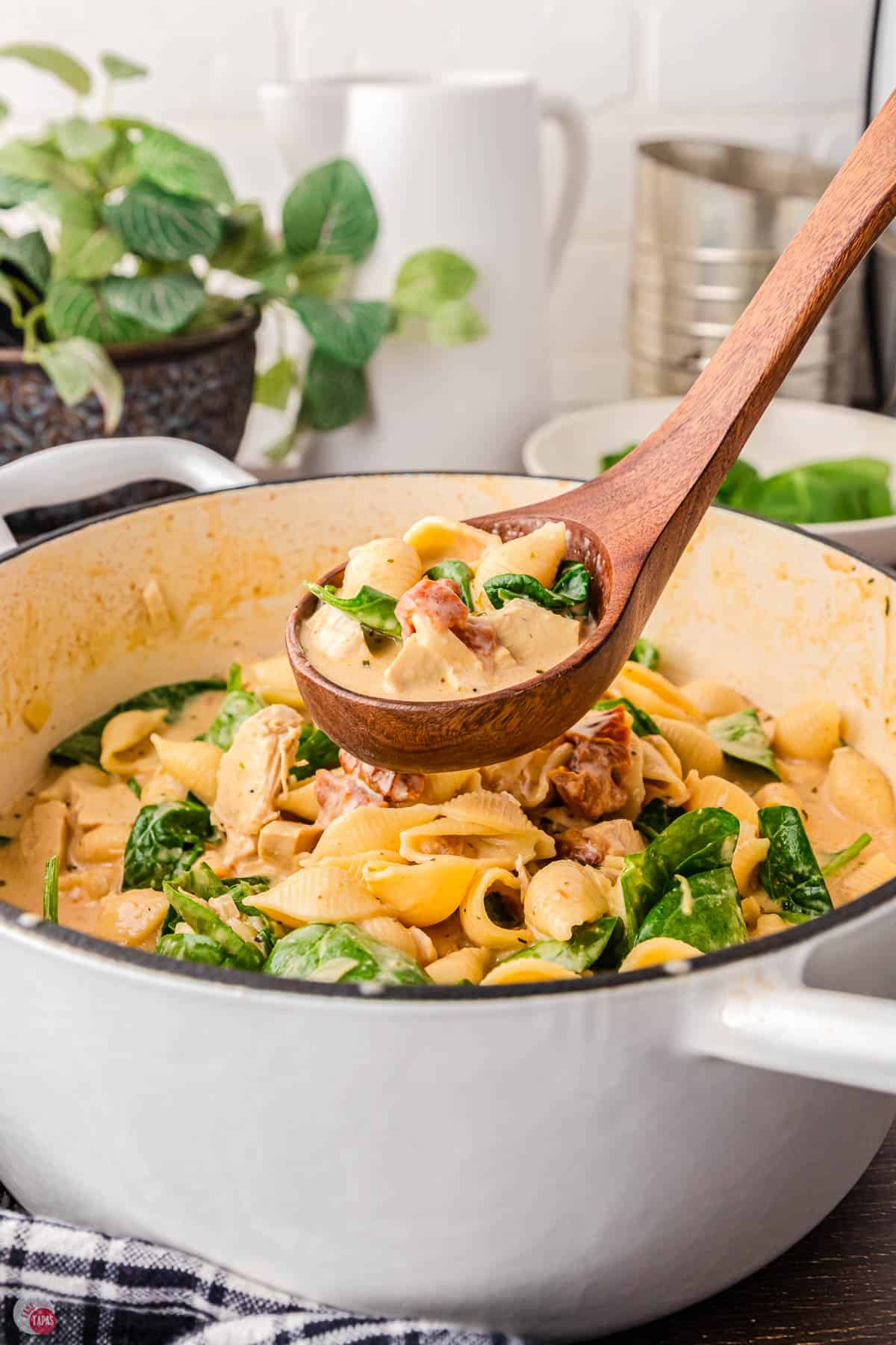 pot of pasta soup with spinach and a brown wood spoon