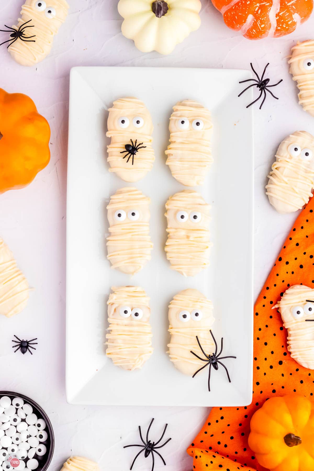 mummy cookies on a white serving tray with a black spider on it and an orange napkin