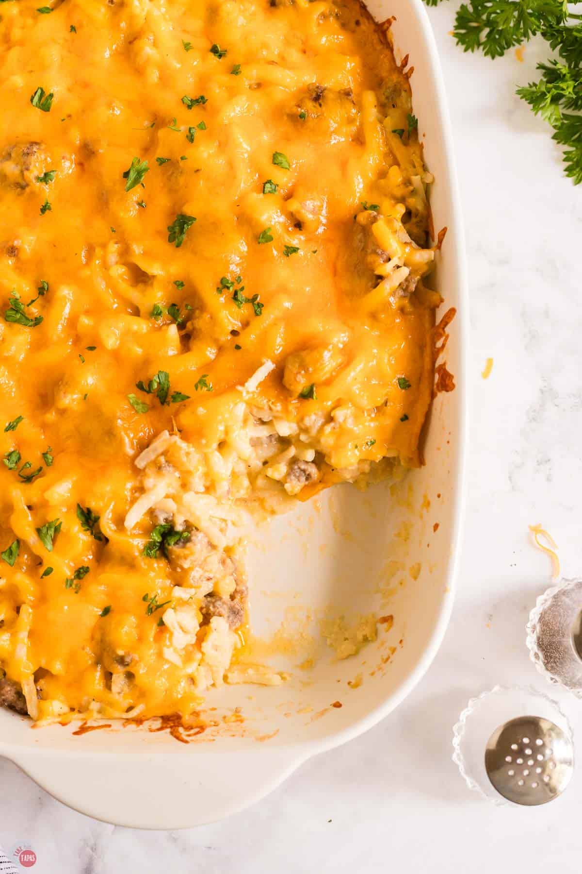 close up of sausage and hashbown casserole in a white dish with a scoop missing