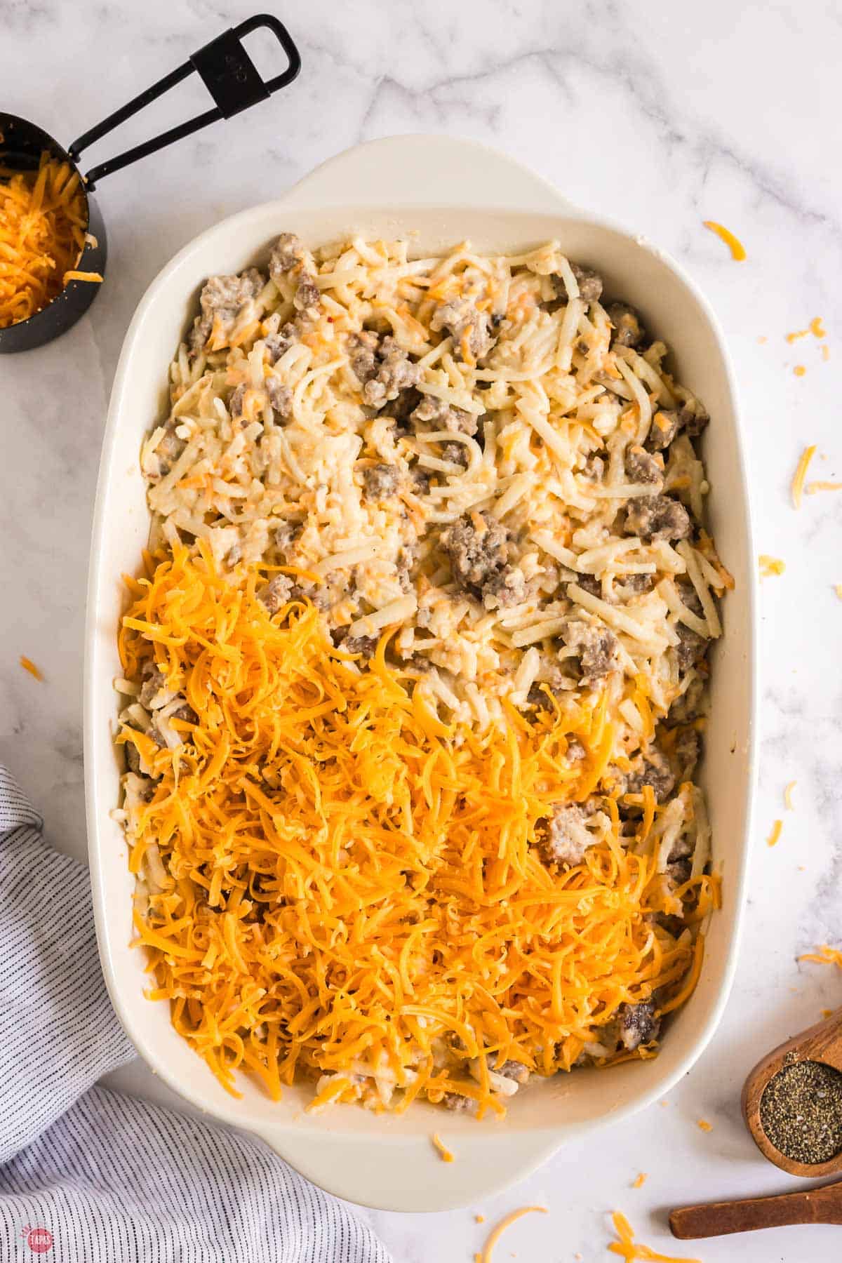 meat and potatoes in a white casserole dish partially covered with shredded cheese