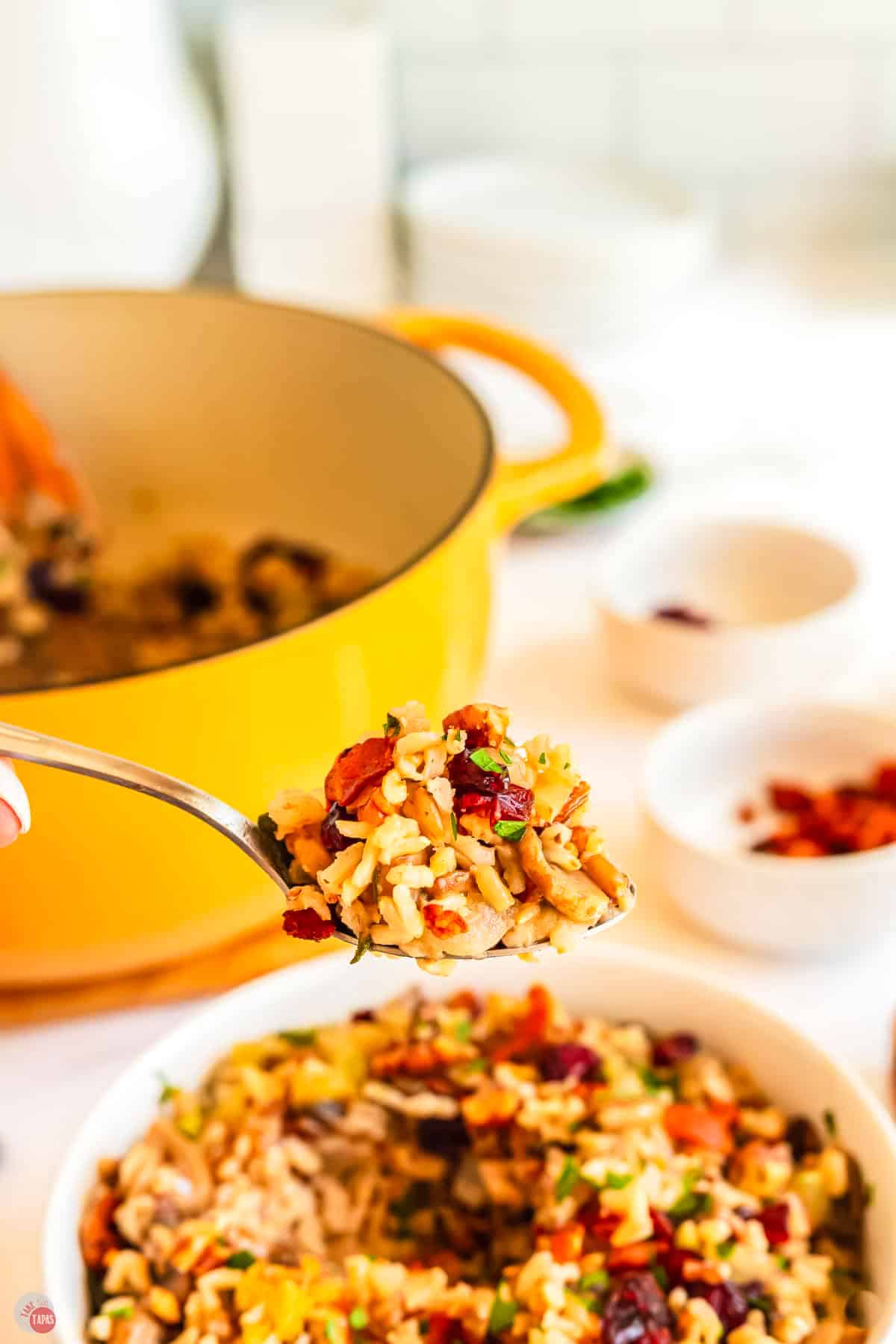spoon with a scoop of stuffing hovering over a bowl with a yellow pot in the background