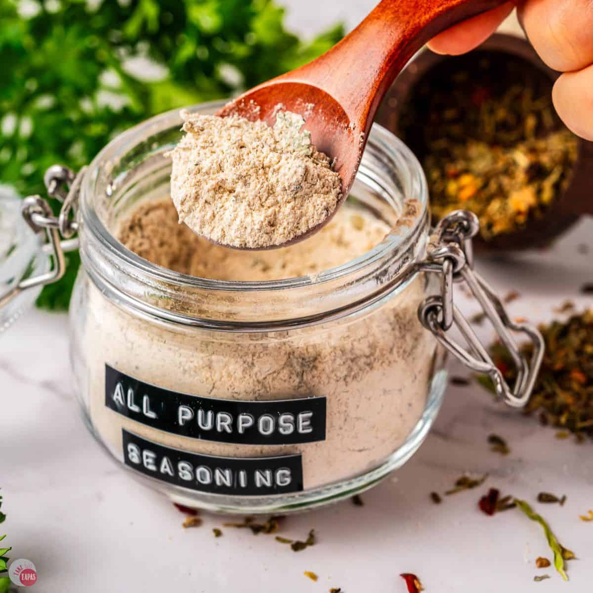 small clear jar of spice mix with a wood spoon