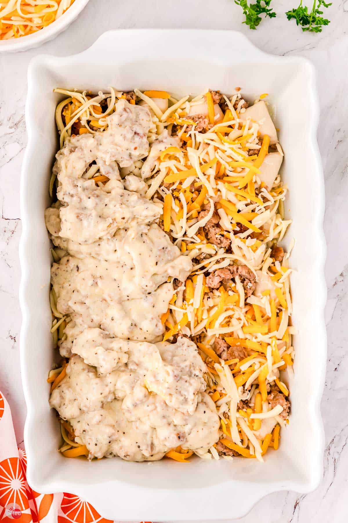casserole dish filled with biscuits and cheese and half topped with sausage gravy