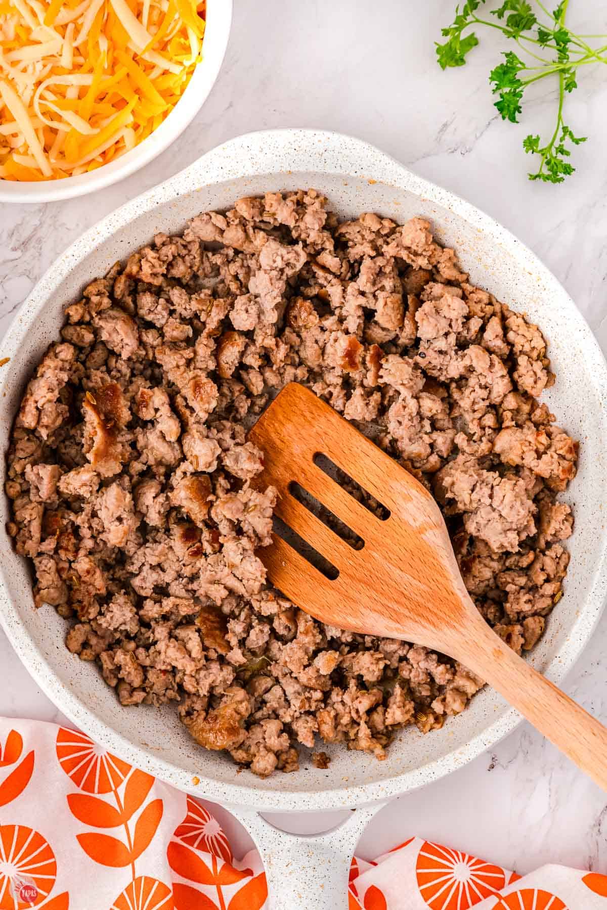 ground pork sausage cooking in a skillet with a wood spoon