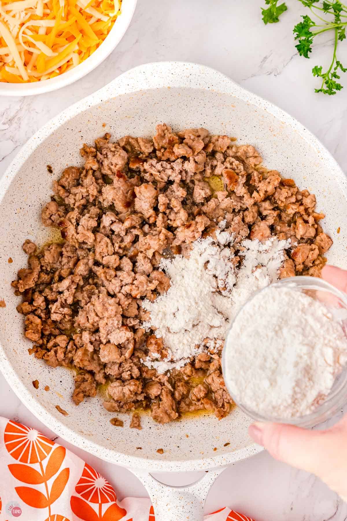cooked pork sausage in a skillet with flour being sprinkled on top