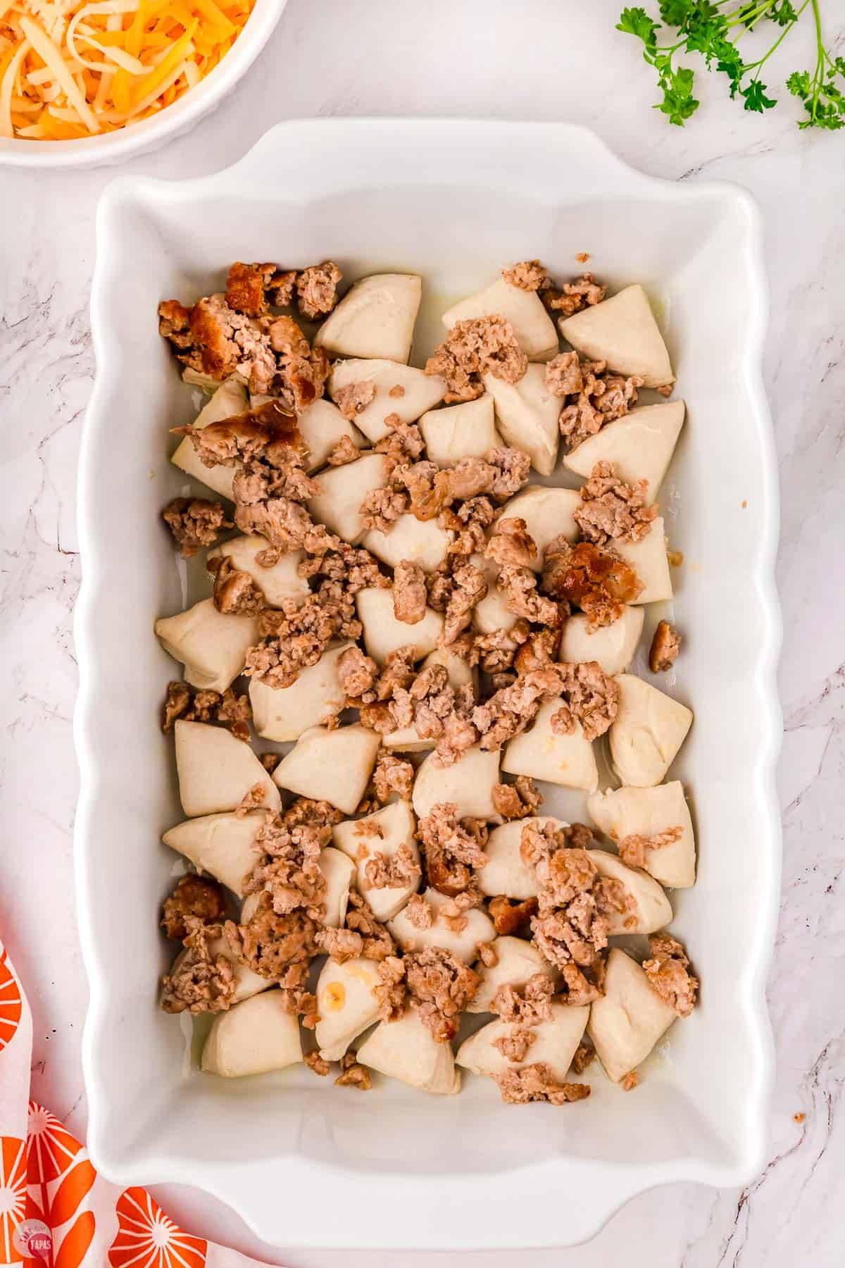 cut biscuits in a casserole dish with cooked ground sausage on top