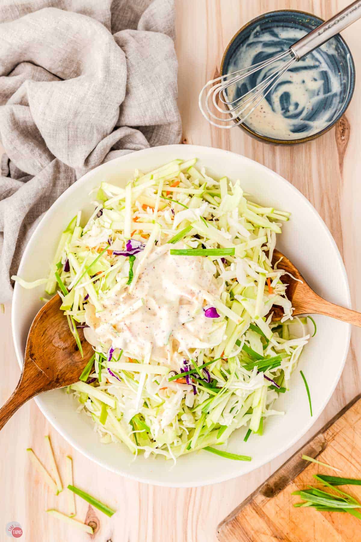 bowl of shredded cabbage with two wood spoons topped with dressing