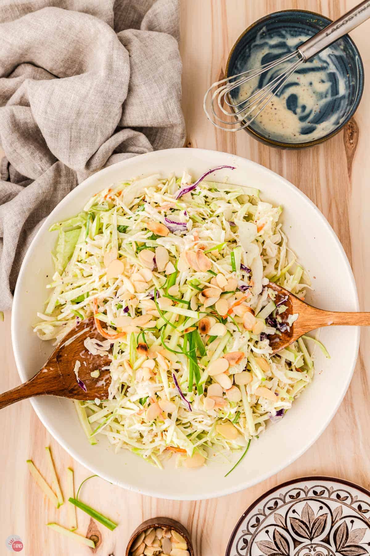 bowl of cabbage apple slaw with two wood spoons